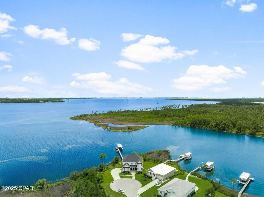 This custom-built waterfront retreat is more than a home; it's a private resort with panoramic bay views, a boat lift with rare DEEP WATER ACCESS, and a show stopping game room unlike anything else. Presiding over North Bay, this home offers expansive living and soaring ceilings. This luxurious residence enjoys a quiet location set back from the street at the end of a cul-de-sac. Built in 2021, the home offers a magnificent game room/den complete with an island bar, dining area, pool table, and space for a home gym, tabletop games, and indoor ball sports. Multiple TVs provide the ultimate viewing for sports fans. Garage-style glass doors fully open to allow refreshing breezes indoors when dining on this level. As you approach the home, a broad staircase leads up to the main level. LVP flooring flows seamlessly through the open living space, formal dining area, and a spacious sitting room. Every seat has stunning views across the bay. A soaring volume ceiling with clerestory windows enhances the space and brings in an abundance of natural light. Gather around the gas fireplace after dinner and enjoy quality time with family and friends. The tall chimney wrapped in shiplap is the focal point of the living room. Lit by three pendant lights, the generous island announces the chef's kitchen, which is equipped with KitchenAid appliances, including a double oven. A pot filler is conveniently located above the smooth top range, ready for pasta nights. A walk-in pantry, laundry, and a wine bar make this the perfect home for entertaining. A wall of windows delivers sweeping bay views, which only get better when you step through the French doors onto the large covered composite deck. From the porch a staircase leads down to the manicured backyard. The primary suite is also on this floor and boasts a boutique-sized walk-in closet and beautiful bay views. The ensuite bathroom impresses with shiplap walls, a dual quartz-topped vanity, and a walk in shower wrapped with tile and glass. A neat makeup area completes this private haven. A guest bedroom, suitable for use as an office, and additional full bath completes the main level. Connected by a galleried walkway, the top floor comprises five additional bedrooms and two full bathrooms, as well as a bonus room. Doors open directly onto another full-width covered porch showing off the best views of the property. Where better to sip cocktails while toasting the sunset over the bay? The home features a two-car garage on the main level and an additional one and a half car garage on the lower level. A community pool offers more recreation beyond boating, fishing, kayaking, and paddle boarding from your private dock.