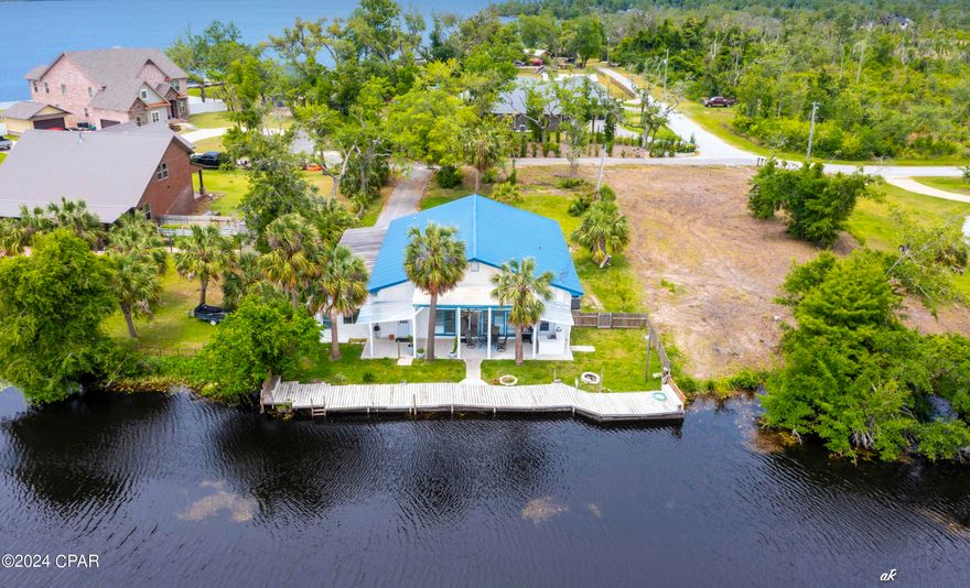 Just imagine living in a lakeside cottage with such a unique and historical history...In the early years, this bayou was part of the Gulf.  The Deerpoint Dam was built in the early 60's creating a spring fed fresh water supply for the Panama City area. Per previous owners, the original structure was a boat house that was used to unload shrimp boats.  After the creation of Deerpoint Lake, the business ceased operation & the structure was approved for a residential property. All the beauty that surrounds the water and property is full of wildlife. The dock was rebuilt over the original frame work and continues into the back yard as a deck. Annually, the water level of the lake is dropped 2-3 ft in Nov where it remains until March when it is returned to summer levels w/the water off the dock at approx. 6-7 feet.  
The living room features lots of windows overlooking the water.  An open floor concept w/large kitchen featuring two side by side refrigerators for the serious chef.  The dining room has a wine closet w/wine refrigerator.  In addition to a large master bedroom /ensuite & walk in closet, there are two other bedrooms w/guest bathroom.  Laundry room is large w/sink, cabinets & shelves.  A workshop is located at the rear of the carport.  All copper wiring. HVAC replaced in 2022. Septic system installed 2017. The yard was graded and sodded to sidewalk level. Gradings and berms were designed to control water flow from excessive rains towards the lake. Septic pumped/checked last year. Two tankless water heaters were installed w/in last few years. Well pump, holding pressure tank & filter system less than 3 yrs. New water treatment system. Electric panels/subpanels replaced in recent years. Assumable sentricon system w/Brock Pest control. Call your favorite Realtor today for a private viewing!  (All important details should be verified by the appropriate specialist.)