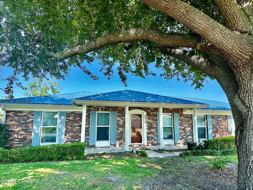 The moment you see this home with its beautiful oak tree welcoming you into the front yard, the quality and elegant traditional features make it stand out from all the rest.  Plus, the location-- situated just across the road from the high-end Sweetbay neighborhood (brand new shopping, marina, and University Academy Charter School) and super-convenient to Gulf Coast Hospital and the stores, restaurants, and entertainment on 23rd St., you will have all the best of Panama City at your fingertips. All of the main roads to reach other parts of town-- Panama City Beach, Lynn Haven, Downtown, St. Andrews, and Tyndall Air Force Base are conveniently close by.  The home itself was renovated after Hurricane Michael and has many new updates in addition to its original solid, quality construction.  The all-brick exterior is capped with a metal roof that was installed in 2019, as was the air conditioner, new plumbing, wiring throughout the home, and several of the appliances. Other features include exquisite scraped-wood LVP flooring throughout, ample closet space, a sunny bay window with a window seat, and extensive built-in shelving to display your books and treasures. There are two spacious bedrooms on one end of the house, one with a private bath and the other with a built-in desk/study/sitting area. On the other end of the house, an 18x17 room with a bay window and extensive built-in shelving that can serve as a third bedroom or a large family room. The kitchen has solid-surface countertops, a large breakfast area, small breakfast bar, and a window overlooking the oversized, privacy-fenced backyard.  Out back you'll find an open patio, a yard building for your toys, and a variety of fruit trees (blueberry, kumquat, fig, lime, and pomegranate).  This home has been meticulously cared for over the years; it comes with a transferrable termite bond and HVAC maintenance plan. Absolutely perfect for retiree or small family! (Seller may consider selling some of the antique furniture separately.)