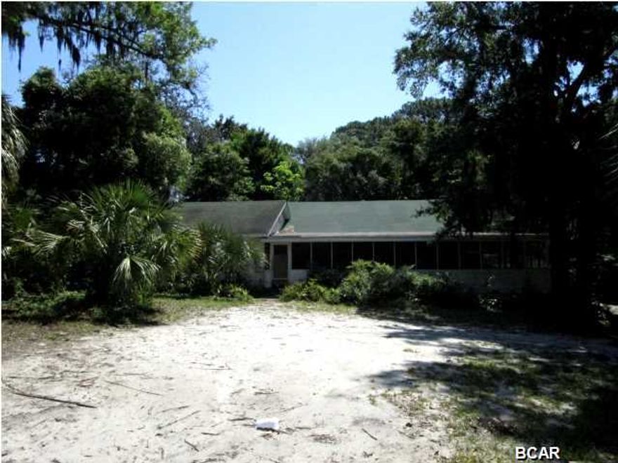 LOADS OF POSSIBILITIES IN THIS ST. ANDREW'S HOME AND JUST STEPS TO THE BAY! With a large screened porch along the entire front of the home, features include a large Family room with hardwood floors and a stone fireplace, an adjoining kitchen and dining area, and a separate office or work area. The Master bedroom has a small Master bath, and one additional bedroom has access to the enclosed porch along the south side of the home, which also connects to the screened porch. Situated on over an acre, the backyard is a tree-filled natural setting with small paths to enjoy! Home is being sold in its AS IS condition.