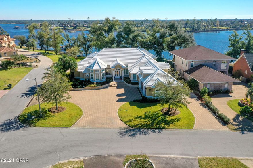 Exquisite waterfront estate in the Panama Country Club in Lynn Haven. The interior of this home features hard wood floors, plantation shutters throughout, filled concrete block construction with stucco overlay & some of the best waterfront in Lynn Haven. The grand entrance opens up to a formal living/dining space with fireplace & built-ins overlooking the brick paver back patio through 3 sets of French doors. The master suite includes floor-ceiling mirrors in the dressing area, double sink vanity with soft close hinges, large tile shower, & makeup vanity. Inside the master bedroom you will find his/hers walk-in closets, tray ceiling with ambient lighting, sitting area with built-in bookshelves, and sliding glass doors overlooking the water & patio. The kitchen includes a surplus of cabinets & counter space. Kitchen is open to the great room and dining space and all have amazing views of the water.  Great room opens up to a covered portion of the patio with access to the exterior half bath & buffet area with sink. The additional bedrooms have walk-in closets and an ensuite bath. Above the garage is a heated/cooled bonus room that is perfect for storage or creating a loft. The exterior of this home features views of Beatty Bayou from a private boat dock with dual lifts. Dock is constructed with composite decking to avoid the wear & tear of natural wood. It has an extra wide dock and walk-around lifts. The left is rated to lift up to 6,000 lbs, and the right is rated to lift up to 16,000 lbs. Power & water are both also available at the end of the dock. This home sits on a corner lot, has a circle brick paver driveway, custom wrought iron fence around the back yard, a fire pit, boardwalk along the water's edge, & lush landscaping.