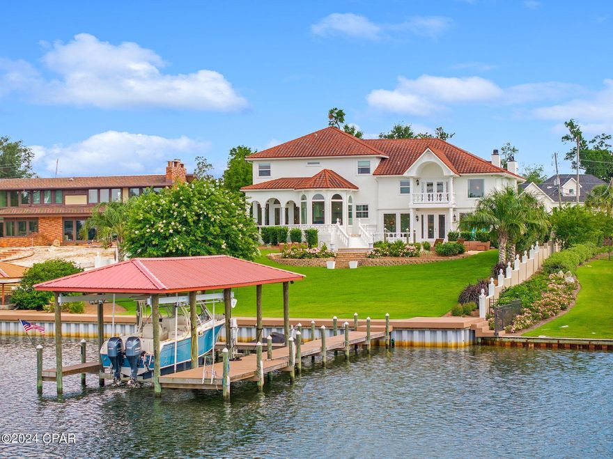 Experience unparalleled luxury and exquisite waterfront living at 1309 Bayou Ct, in the prestigious Cove community of Panama City, FL. Constructed with durable block and finished with a refined stucco exterior, this expansive 5-bedroom, 5-bathroom residence offers elegance and comfort in over 5,510 sq ft of meticulously maintained living space, situated along 100 feet of deep bayou waterfront--ideal for boating and water enthusiasts, and only minutes by boat to Shell Island. Step inside through the 12-foot custom solid iron front doors and be welcomed by a grand foyer with soaring 21.6-foot ceilings, illuminated by a stunning RH Foucault's Crystal Orb Chandelier. Stunning elegance flows throughout this well-appointed home, featuring Italian travertine floors, intricate crown moulding, and two inviting fireplaces in the family room and formal living room, creating warmth and an inviting atmosphere for gatherings. The gourmet kitchen has been thoughtfully updated recently with top-tier Wolf double ovens and gas stovetop, Sub-Zero refrigerator, and Cove dishwasher appliances, granite countertops, and an island with breakfast bar seating. The light-filled breakfast area offers panoramic views of the bayou and pool--setting the perfect scene for your morning coffee. The primary master suite is a private serene sanctuary, complete with a private balcony overlooking the pool and bayou, a stately fireplace, and a unique 84-inch dome ceiling with a crystal chandelier. The spa-like master bath features an oversized tub, separate shower, double sinks, and space is available for built-in conveniences like a mini-fridge, microwave, and TV. In recent years, over $185,000 has been invested in thoughtful improvements. These include a new seawall with heavy-duty tie bolt anchors, upland Moisture Shield decking on top of the seawall, a new metal roof for the boathouse, and new dock decking (2021). The backyard was completely redesigned with new landscaping, large palm trees, and an updated irrigation system, creating an outdoor space as inviting as the interior. Additional updates include a freshly repainted exterior (May 2024), a new two-unit HVAC system (January 2024), and a new pool heater, spa pump, and pool pump replacements (Fall 2021). With a circular driveway, grand fountain, in-ground pool, and spacious drive-through two-car garage, this home offers a seamless blend of elegance and convenience. Surrounded by mature trees and situated in one of Panama City's most sought-after neighborhoods, this residence exemplifies luxury living at its finest. Ask your agent for a complete list of upgrades and renovations done in recent years, and schedule your private viewing today to explore all that this exceptional property has to offer. All information is deemed reliable but not guaranteed; buyers should verify if important.