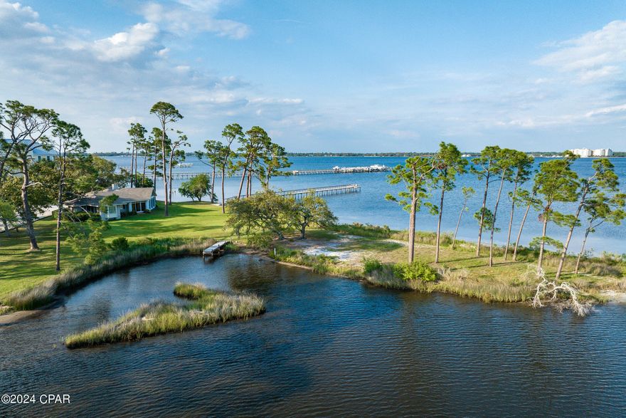 This property has sold! Discover similar listings by reaching out to us for an updated list of available properties that match your preferences. This is one of the most impressive pieces of waterfront real estate in Panama City Beach. Keep the existing homes (main house and guest house) or redevelop into a modern, grand estate.
------------  Nestled amid lush pines, oaks and magnolias, ''Fiddler's Green'' is a serene haven set on 2.98+ acres of coastal paradise. With an incredible 800 feet of water frontage, this idyllic retreat offers unparalleled views and direct access to enjoying fishing and boating in St. Andrews Bay, the Gulf beyond, or in the bayou out back. In 2005, the home was remodeled to enhance and modernize it for gracious living and easy entertaining, and now features a two-level, fan-shaped living room that elegantly divides the house into two distinct wings. Each of the three bedrooms, with private bath, is tucked within its respective wing to provide personal sanctuaries. The heart of the home lies within the spacious great room, seamlessly blending living, dining, and kitchen areas, anchored by the huge fireplace on one side and the copper-topped bar on the other. The standout feature is the expansive window wall, offering 180-degree panoramic views of the ever-changing sky, water, and shores from the comfort of home.  Parades of fascinating watercraft enliven the water scene, while birds, deer and dolphins make regular appearances. With no HOA to restrict your lifestyle, a separate guest house, and a truly unique parcel of land, this extraordinary property stands as a rare find in the market. Aptly named for the perpetual joy it evokes, Fiddler's Green offers both seclusion and convenience. While providing privacy and peace, it is also just minutes away from St Andrews State Park, Bay Point amenities, and a plethora of the area's best restaurants. Schedule a viewing today to experience the romance and the magic of ''Fiddler's Green'' firsthand.