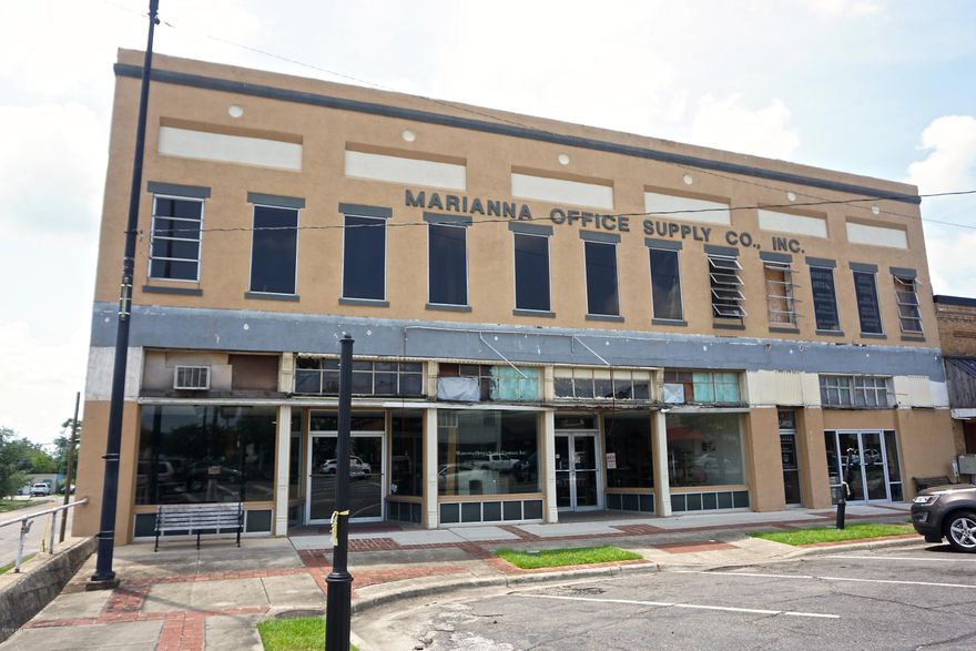 GREAT INVESTMENT OPPORTUNITY for someone with VISION!! Historic commercial building in downtown Marianna on Hwy 90 that was Marianna Office Supply for many years. Located right in the middle of the retail district. It has great bones, but needs some TLC. The building is located on a corner lot that is accessible by a service road with parking off of the highway. The main floor is a large open warehouse style room with display windows and high ceilings, two private offices, one open air office, and two bathrooms. The upstairs is breathtaking with  exposed brick, original tongue and groove floors and ceilings, and many windows with the best views of downtown Marianna. There is an old (non-working) elevator, a large basement with outside access, and other adjacent large office building. The adjacent office is approximately 2,300 sq ft with its own entrance, bathroom, office, basement, and upstairs. There is a firewall in between the two. The roof has been replaced since the storm.