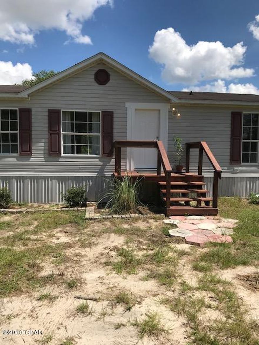 This large mobile home comes with a little over three acres. The land goes beyond the fenced in the back yard, all the way to the tree line in the back and several feet beyond. The home comes with a $1,000 flooring allowance if the price is right. Mobile home is being sold as is. This would make someone a wonderful home out in the country. There is room for your horses and a garden. Set on your back covered deck in the evening with a cool glass of tea. Very nice mostly cleared lot. The time to buy that home is now. The home has a living room, and a separate den with a fireplace. The bedrooms have a split floor plan, with the large kitchen dividing them. With a little work you can make this large mobile home your piece of paradise.