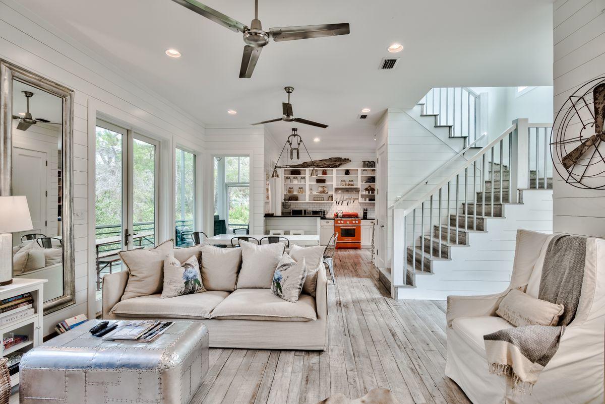 With a coveted location between WaterColor and Seaside, the Hammocks at Seagrove is a peaceful gated community nestled among large magnolia and oak trees. This custom-built home boasts shiplap walls, hand scraped hardwoods, and high ceilings which maximize the natural light.  The main level provides open-concept living with a cozy indoor fireplace and bright coastal decor. French doors open to a large screen porch for dining al fresco or relaxing after a day at the beach. The dining area has a custom-made dining table that comfortably seats 8. The kitchen has a breakfast bar, open shelving, and custom grade appliances  from The Big Chill designer series. The second level has floor to ceiling windows surrounding an additional living area with two couches for entertaining.