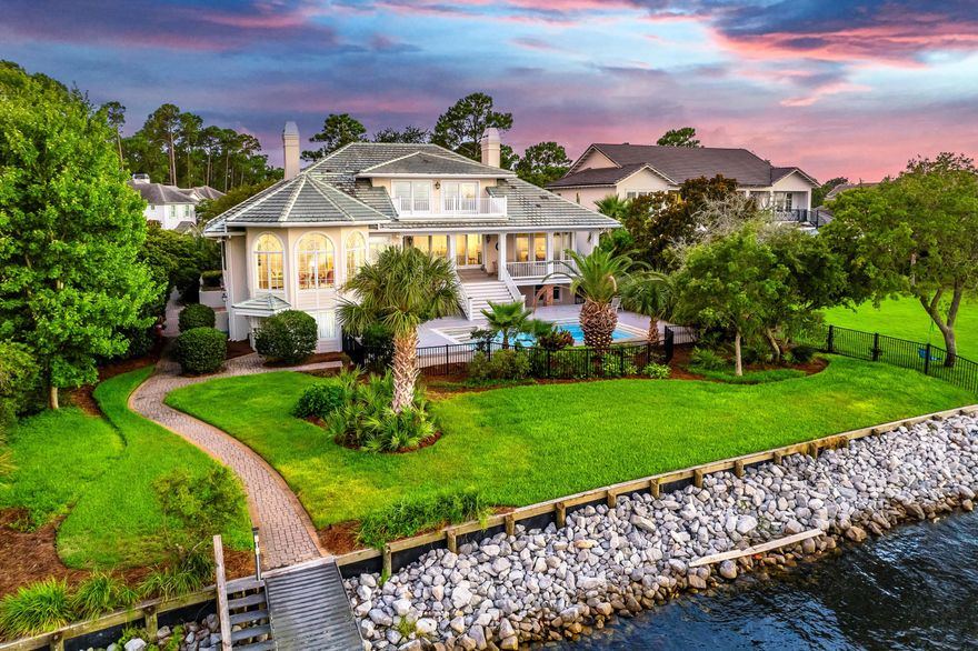 Timeless elegance on the bay behind the gates of prestigious Regatta Bay Golf and Yacht Club. This enchanting sanctuary sits surrounded by lush, mature landscaping, perched over 108' of water frontage with endless bay views. Remarkable in detail with deep porches and graceful design, it exudes a sense of grandeur while embracing impeccable craftsmanship and tranquil comfort. Reminiscent of Louisiana low-country homes, Prescott Architects' raised design highlights water vistas from every vantage point. A rare combination of warmth and space, it measures over 6000 square feet in heated space with over 1000 square feet of porches. Enter a commanding facade to a grand entry which reveals impeccable inlaid marble flooring joined by immaculate hardwoods.