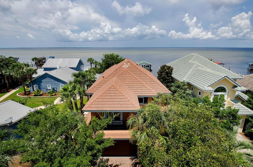 Well-designed Bayfront home with 60 linear feet of water frontage yields panoramic views of the Choctawhatchee Bay at every turn. Nestled among lush greenery, a two-story enclosed outdoor living space with well-equipped summer kitchen with icemaker, pool, hot tub, sitting area, and alfresco dining area beckons calm Bay waters and offers exceptional privacy and serenity. The dock leads to a boatlift and 2-story boathouse. The boathouse is shared with neighboring home, but the docks are separate. Sweeping views of the Bay flow artfully throughout the home's wide expanse of windows, while the open floor plan mimics the breezy open-air feel of the surrounding landscape. This finely appointed showpiece includes raised ceilings, deep crown molding, and 18'' tile set on a diagonal. With stainless GE appliances, 5-burner stovetop, granite counters, breakfast bar with seating for 6, and built-in buffet, the spacious gourmet kitchen will impress the most discriminating epicureans. The living room with 2-story ceiling offers built-in shelving, access to the patio and pool, and a focal-point gas fireplace. This home affords two master suites, each with Bay views. The first floor master suite opens to the pool area, while the second floor master leads to a Bay-facing balcony. Both master baths feature whirlpool garden tubs, walk-in shower, dual vanities and twin closets. The second floor is dedicated to guest suites, including a loft bedroom, which is currently used as a sitting area. Additionally, this home offers a new hot water heater, dual A/C, and a large garage with storage closet. This desirable Miramar Beach location provides quick access to shopping, dining, and entertainment.  
