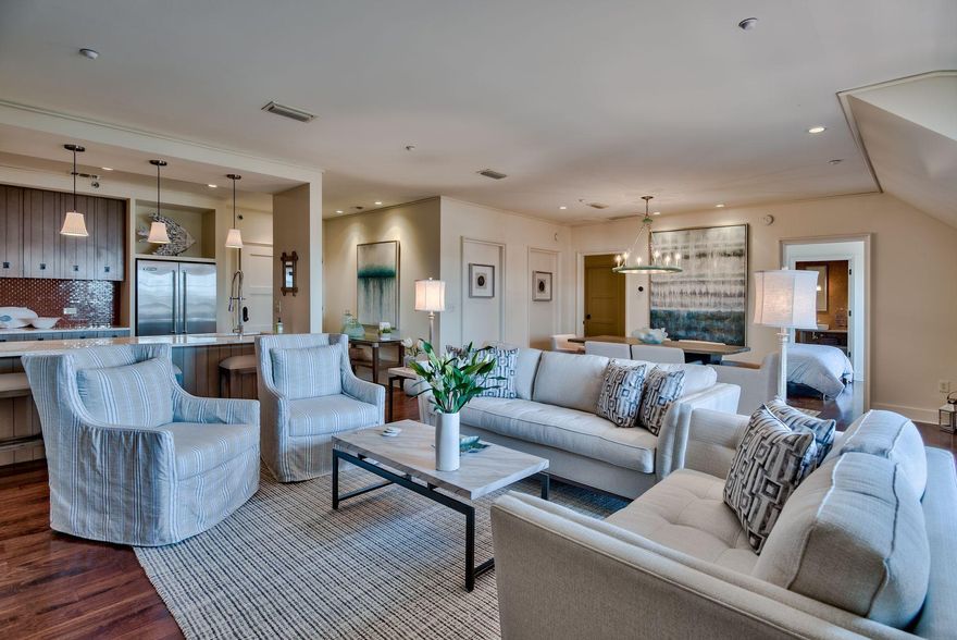 Interesting architectural detail and gorgeous hardwood flooring adds character and charm to this Rosemary Beach Barrett Square condo. Open plan living provides a bright and airy spaciousness as the day takes you from bagels at the breakfast bar to late night movies on the TV console in the living area. French doors stand open to provide fresh sea breezes and access onto the balcony; it's a peaceful place to relax with a drink and watch the world drift by below. The kitchen has a full range of upper and lower cabinets, white marble countertops and stainless steel appliances beneath a tray ceiling. A contemporary chandelier lights the dining area for entertaining dinner guests or game nights with friends and family.