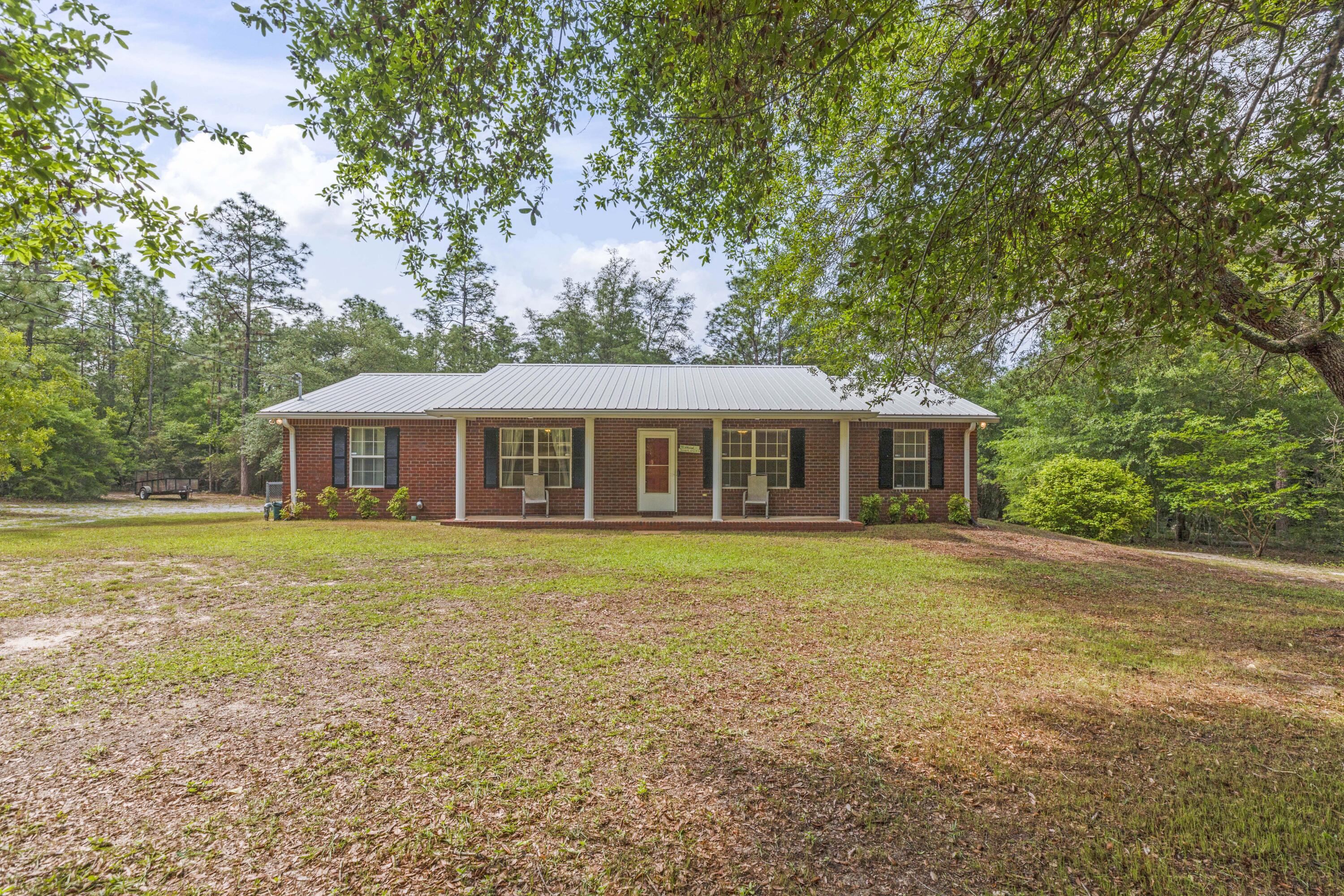 COUNTRY LIVING AT ITS BEST! Beautiful ALL BRICK 4 bedroom 2 bathroom with METAL ROOF on nearly 4 ACRES of LAND in north Crestview! This lovingly maintained property offers both space and privacy while being close to the convenience of north end shopping and schools. As you approach the home you are guided back to the home by a private gravel driveway nestled through the trees. The front of the home offers a covered front porch, perfect for rocking chairs. As you enter the home, you are greeted by a small tiled foyer with plenty of space for an entry table. Off to the right, you will find the homes formal living room and dining room with wood laminate flooring to entertain your guests. At the end of the foyer, you are guided to the homes main living area. The spacious family room with wood laminate flooring offers views of the back yard and covered deck. This room also connects to the homes second dining area and kitchen. The spacious kitchen is complete with ceramic tile, plenty of wood cabinets and counter space, refrigerator, stove, dishwasher, and microwave. The kitchen also has a convenient pass through to both the dining room and dining area. Down the hallway, you will find all of the homes bedrooms. The master bedroom, located at the end of the hall offers both space and privacy. The master bedroom can easily accommodate a king bed and has its own closet, ceiling fan, and private full bathroom. Bedrooms 2, 3, and 4, are all spacious in size with generous closet space and ceiling fans. All bedrooms have new Stainmaster carpet. Just off of the living room, a set of French doors takes you to a large covered deck overlooking the beautiful back yard. A large portion of the cleared back yard has a chain link fence perfect for pets or children. The property has plenty of wildlife to enjoy, such as deer, turkey, rabbits, squirrels, and birds to name a few... The back yard has two outbuildings to enjoy, one on a slab, and one with power. This spacious 3.97 acre property has all of the space for peace and privacy that you will need and plenty room for that boat or RV. The wooded front and back portions of the property nestle this home in perfectly, giving you the ultimate feeling of privacy. The exterior of the home also offers metal roof and gutters, irrigation system, and more... The opportunity at finding a property of this price, quality, size and feel does not come along very often. Don't let this country beauty slip through your fingers. Schedule a showing TODAY!