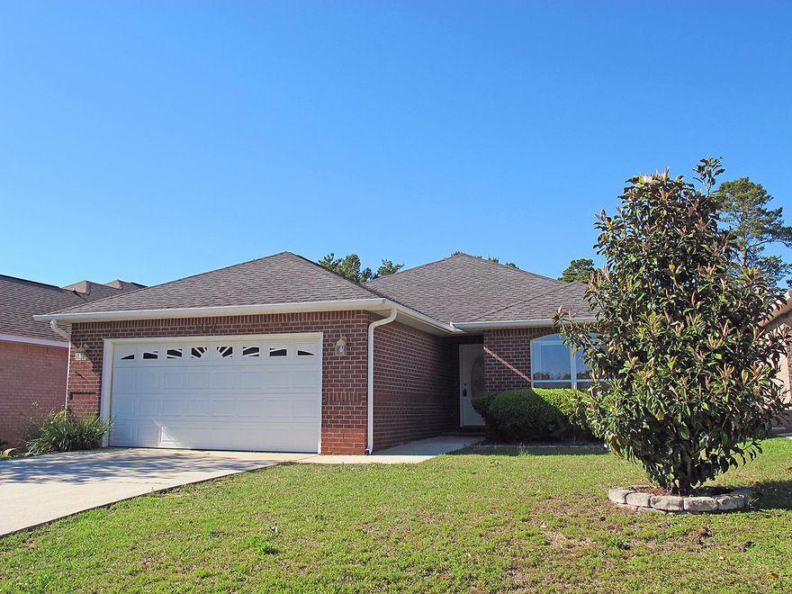 Such a charming home! Located in the quiet, upscale Oak Pointe subdivision, south of Hwy 98 and part of the Tiger Pointe area, and an easy drive to Pensacola and the beach. This immaculate home backs up on a lovely green space, is very well-maintained and is move-in ready. An attractive all-brick exterior and hip roof keep your insurance rates lower.As you enter through the lovely front door accented with decorative glass, a spacious living room welcomes you. Plenty of space for comfy sofas and chairs and a large screen TV. The interior features tile and laminate flooring throughout (no carpeting!), and ceilings are textured (no popcorn!). A hallway opens to your right, where two sunny bedrooms are separated by the hall bath. (Continued)