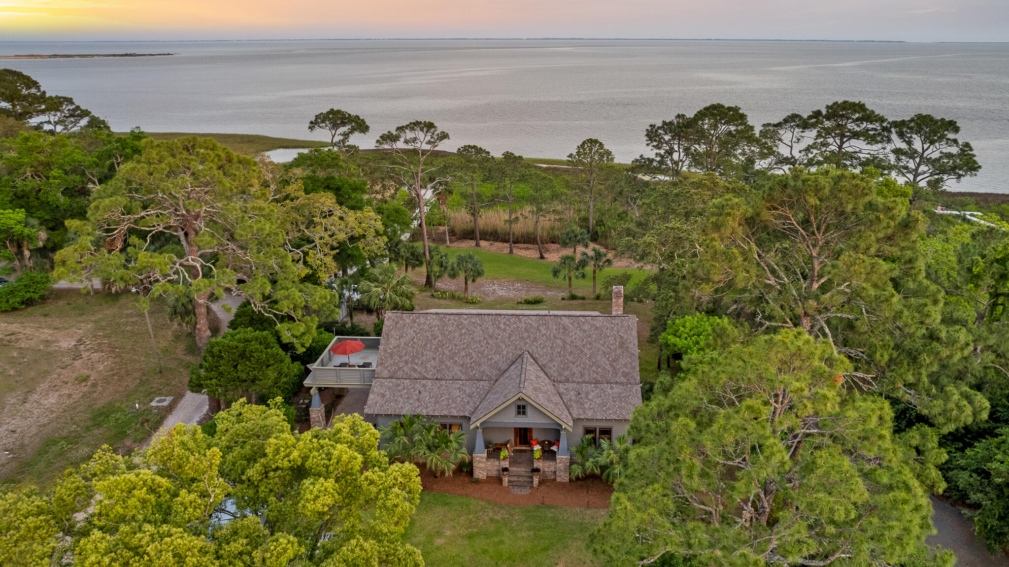 This Exquisite Private Compound, hosts a large, 5 Bedroom, 5 Bath,''Craftsman'' Bungalow on an Acre on the Bay of Apalachicola, with private dock,two guest studios, outdoor ovens, fruit orchards, gardens and spectacularpanoramic views of three barrier islands.This exquisitely CUSTOM ''Arts & Crafts'' Bungalow was built in 2005, by thecurrent owners. The main house is a sculptural masterpiece, built of stick frameconstruction on a slab, with cedar shake exterior, sitting on an acre on theApalachicola Bay, with view of SGI and barrier islands, with guest studios andprivate dock.The interior board and batten paneling, all doors and windows are made of clear,''dead head'' cypress, in the Japanese influenced ''Arts & Crafts'' & ''Prairie Style.'' The owner/builder had antique logs (that had previously fallen off logging barges traveling up the Apalachicola River) pulled from the river by divers and local "dead headers." The cypress logs were aged and seasoned, then custom milled at Santa Rosa Mill Works. The floors throughout the house are of heart-pine and
provide incredible warmth and texture to the walls of one of the downstairs bedrooms, as well. Highly skilled finish carpenters, wood workers, cabinet makers, masons, stained glass artists, each blessed this remarkable home built of rare wood and custom materials. The are custom, hardware and built in mica lamps. The custom details of this gem are evident everywhere you look.
The house has a 5 bedroom, 5 bath floor plan, with an additional room distinctively an office or nursery. The large upstairs primary suite has a sitting room, large walk-in closet, Jacuzzi tub, and sauna. An upstairs stargazing balcony is off the entertainment/den area, which may also function as a sixth bedroom. The dormer spaces are insulated against temperature changes, which makes forlarge storage areas. The two downstairs bedrooms each have full baths. The built-in features arevremarkable; the stairs, staircases, newel posts, benches, bookcases, are all made
of deadhead cypress. The fireplace is framed by handmade "Green Man" art tilesvby an artist in Port Townsend, Washington. The four stained glass windows were fashioned by local Apalachicola artist, Paula Harmon. The kitchen has heart pine cabinets, lined in cedar and the stunning green subway tile, frames a six-burner gas stove. The counters are all hewn from 'heart pine, also, inviting the outdoors in. The chef's kitchen is highly functioning with
stainless appliances. Each floor of the guest house is totally autonomous, with private baths and kitchens. An outdoor free standing brick bread oven sits amongst citrus and fig orchards, organic garden, outdoor pergola and dining. A sweeping front Bay view porch overlooks the compound and the firepit on the Bay, for those memorable family evenings. The compound is home to over 250 species of birds, fish, dolphin, manatee, gators and otters.
Besides its unique beauty, the main feature of the home is its privacy. The property sits on over an acre on the Apalachicola Bay, on nine lots. The dock extends into the bay and is perfect for launching shallow draft watercraft. The property boasts views of three Gulf barrier islands: SGI, Little SGI and St. Vincent.
The house is on a high bluff, with stupendous views from every window. The property has both city and well water sources.