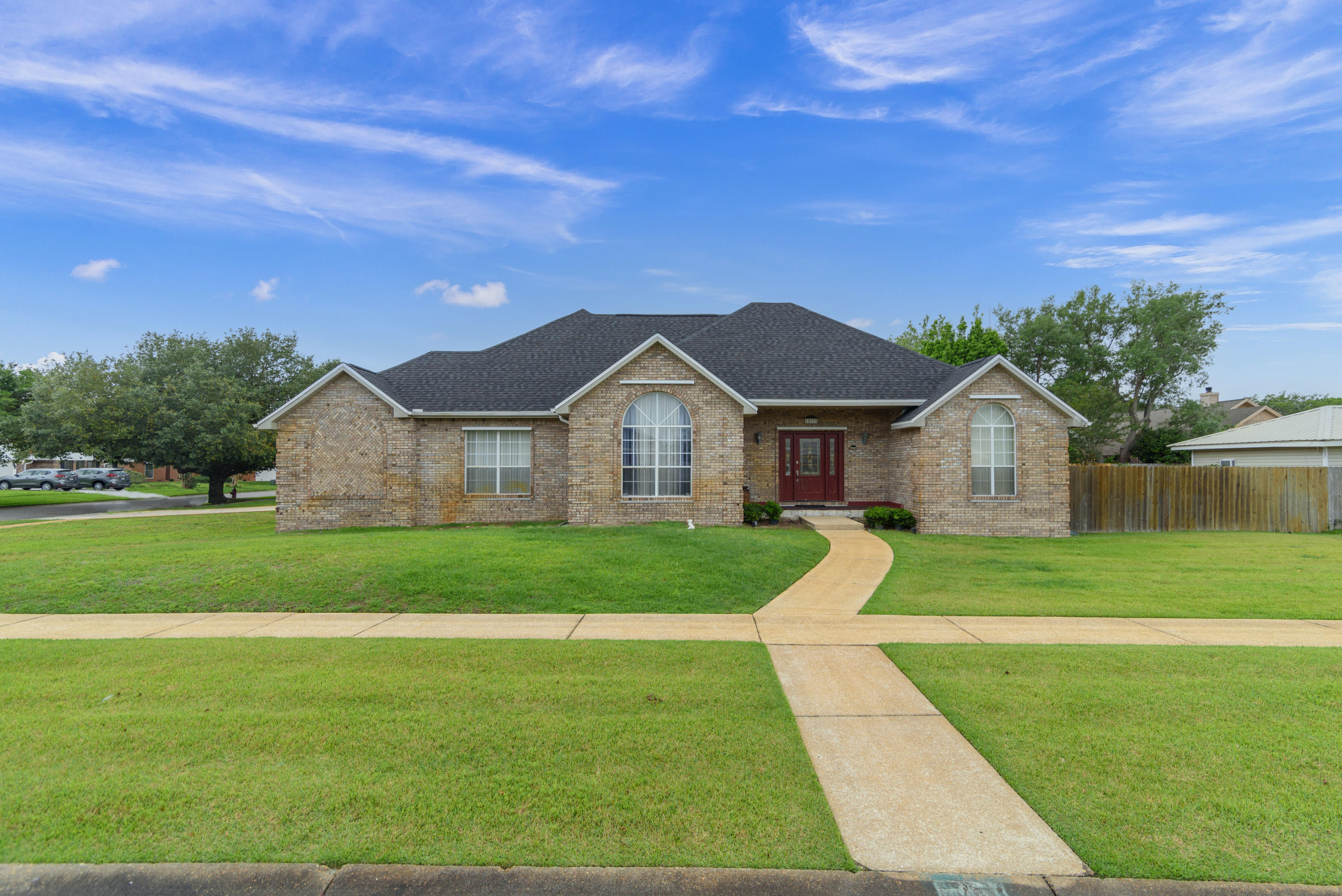 This three bedroom brick home sits on a corner lot in a beautifully manicured neighborhood with sidewalks throughout. Step into the tiled foyer, which opens up directly to the living area, with wood laminate flooring, tray ceilings, recessed lighting and a wood-burning fireplace at the focal point. To your left is a formal dining room with tall vaulted ceilings and real wood floors. The dining area opens to a galley style kitchen with large tile floors, stainless steel appliances and tons of cabinets. A breakfast nook sits opposite the dining area.
Off of the kitchen, to the left, a small hallway has entry to the garage, a laundry room and the main bedroom suite. The main bedroom also has tray ceilings and wood laminate flooring and is quite spacious! The ensuite bath features tile flooring, double vanities, a glass shower, his and hers walk-in-closets on either side of the whirlpool tub and a separate water closet with door for added privacy. A must-have when sharing the bathroom!
This is a split floor plan, with two bedrooms, a hall bath and hall closet in the hallway off of the living room. The bathroom has tile floors and a tub / shower combo. Both hall bedrooms have carpet flooring.
Off of the living area and breakfast nook, two sets of french doors open to a bonus room, perfect for an office, playroom, den, game room or fitness equipment. From the bonus room, another set of french doors opens to a spacious enclosed patio with ceiling fan, looking out to a beautiful "v-shaped" vinyl-lined in-ground pool with a patio big enough for furniture to create an outdoor living area. A privacy fence surrounds the backyard, including the pool, deck and lawn area.
This home is located blocks from the Santa Rosa Sound and minutes from the Navarre Beach Bridge. Multiple golf courses and tourist and family favorites like the Gulf Breeze Zoo are closeby and the shopping, sports, concerts and dining of Pensacola are just a short-drive away. A home with these great features and perfect location won't last long!