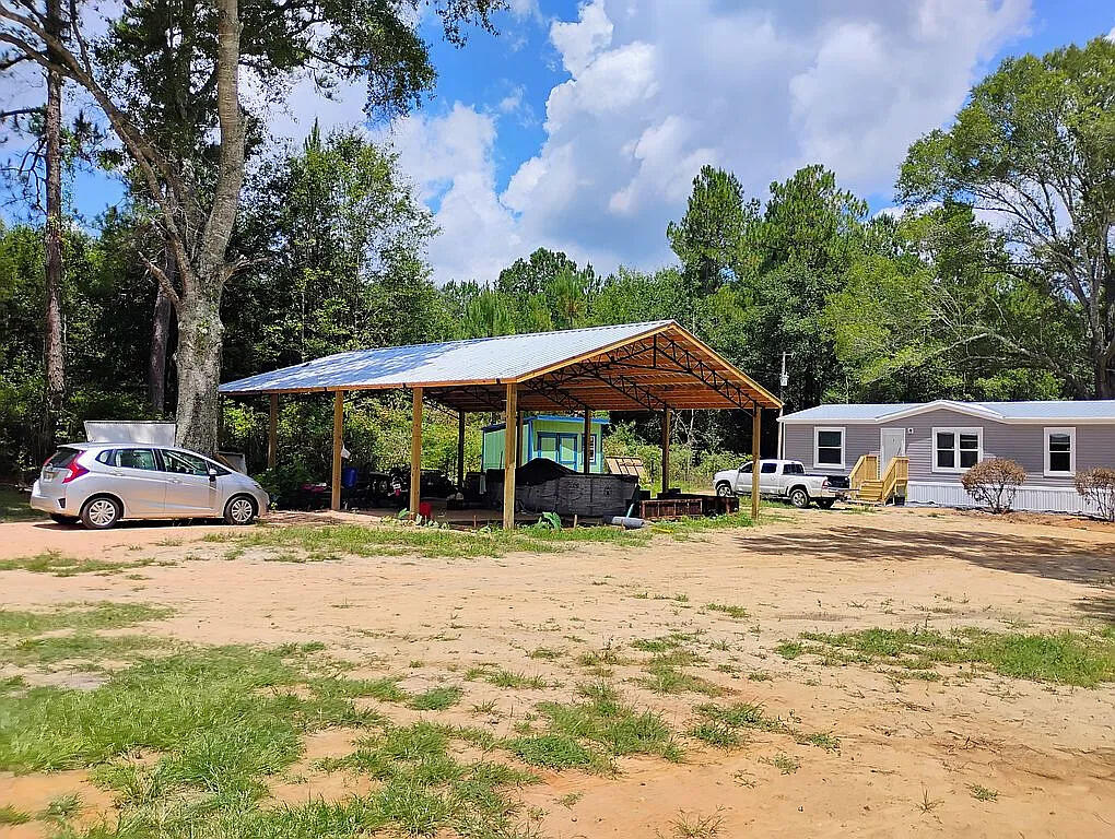 This Timberline 2024 Double-Wide was brand-new when set up at this lot. It is a 28' X 56' (1568 sq ft) 4 bed/ 2 bath home, with metal roofing, & the heat pump moves air from the ceiling, far more efficient than pushing cool air up from the floor. The Zone 2 rating & 2' X 4' construction ensures the home can handle Florida's storms with ease. All windows are double-glazed & equipped with blinds to help keep the heat out. Site-built steps & porches on both front & back are sturdy, safe & attractive. The primary bedroom & bathroom are quite spacious & include a walk-in closet. The additional bedrooms are all roughly the same size & easily accommodate a twin bed, large dresser & nightstand, & still leaves plenty of elbow room, or maybe use one as a home office, with a view of either the pool under the pole barn & the lovely front lawn, or the woods behind the house! This is a very quiet, peaceful setting amongst pastureland, yet within a 15 minute drive you have access to everything you could want in Graceville or Chipley: restaurants, banks, grocery stores, libraries, post offices, clinics & a hospital. The back half of the lot is undeveloped & many large Oak & Pine grow throughout front & back portions...deer have been seen grazing in the back yard, & there is a small crawfish pond near the rear of the lot. The 30' X 40' pole barn provides covered parking for your vehicles, & currently keeps the 16' X 10' X 4' Coleman pool nice & cool!! An 8' X 10' shed gives you a place to keep tools & equipment secure & out of the weather. The fenced yard at the front of the property is a safe place for pets & people to play, & the chicken coop/potting shed combo is a nice low-key hobby farmer's delight, located next to a small garden the provided us with herbs (Basil, Oregano, Parsley, Rosemary, Lemongrass & Sage) squash, melons, sweet potatoes, cucumbers, long beans, tomatoes, peppers, ginger root, and the blueberry/blackberry bushes & grape vine should start producing next year.