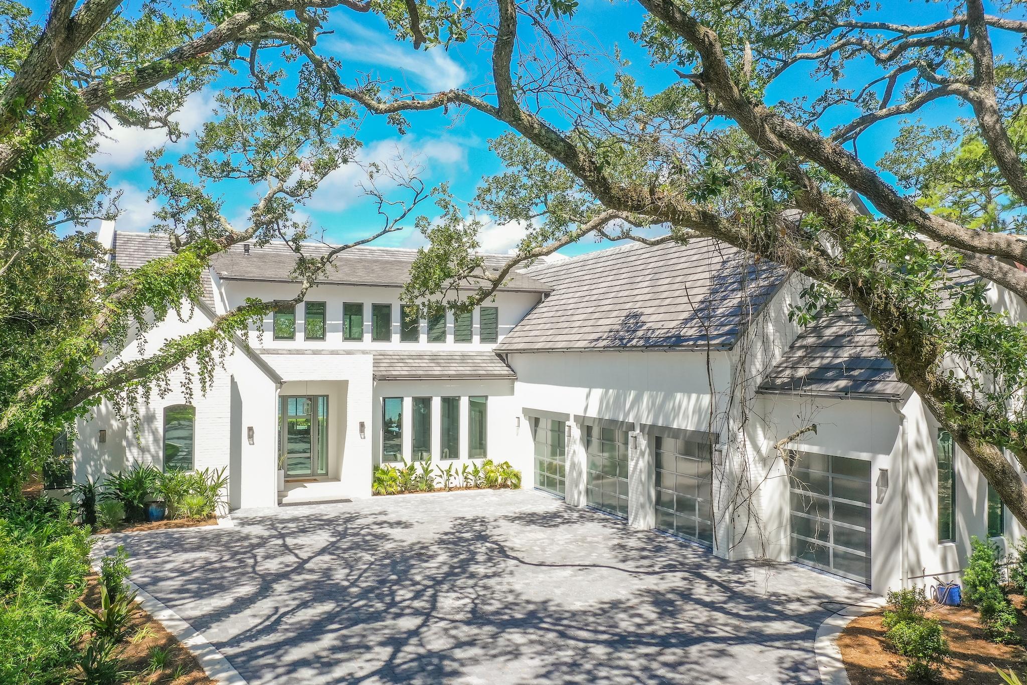 An extraordinary, nearly newly constructed, soft-contemporary dwelling stands poised among a covering of moss-draped live oaks and mature native landscaping. This home claims momentous presence over breathtaking 180 degree Choctawhatchee Bay views and year-round sunsets. A stately white stucco exterior softens under accents of painted brick, and pecky cypress. A dramatic wood and glass fully hinged front door hints at the well-appointed interiors while a 4 car garage is attractively accessed through full-view steel and glass retracting doors. Breathtaking bay views lure visitors through an unforgettable two-story wall of windows and fully retractable glass doors.