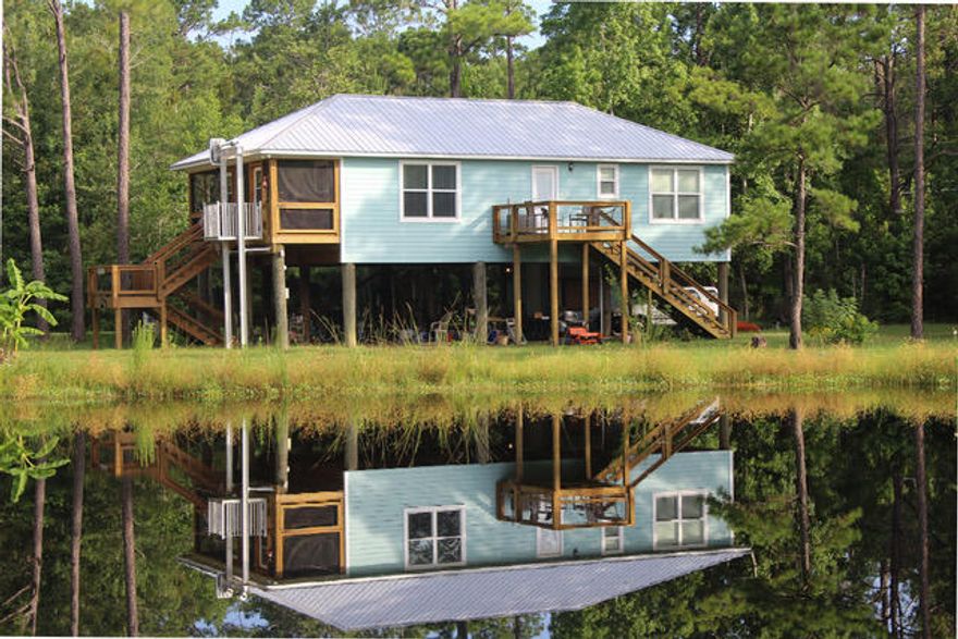 Florida Cottage on .83 acres and your own fishing Pond.Enjoy the Coastal Breezes from your inviting screened porch while watching the sunsets dance across the water. Immerse yourself in tranquility. Nestled in the natural tree top surroundings.  Special attention was given to the details, from the open-concept kitchen and den to the spacious family  island, ideal for serving & entertaining. The primary suite offers a large walking closet, a private bath & custom shower. The 2nd bedroom is spacious with lots of light and also offers a walkin closet.Plenty of  parking space below provides protection and convenience for cars, boats, kayaks, jet skis & water toys. Storage room to house the water toys This set up is designed for every day fun on the water. NO HOA -great investor opportunity.