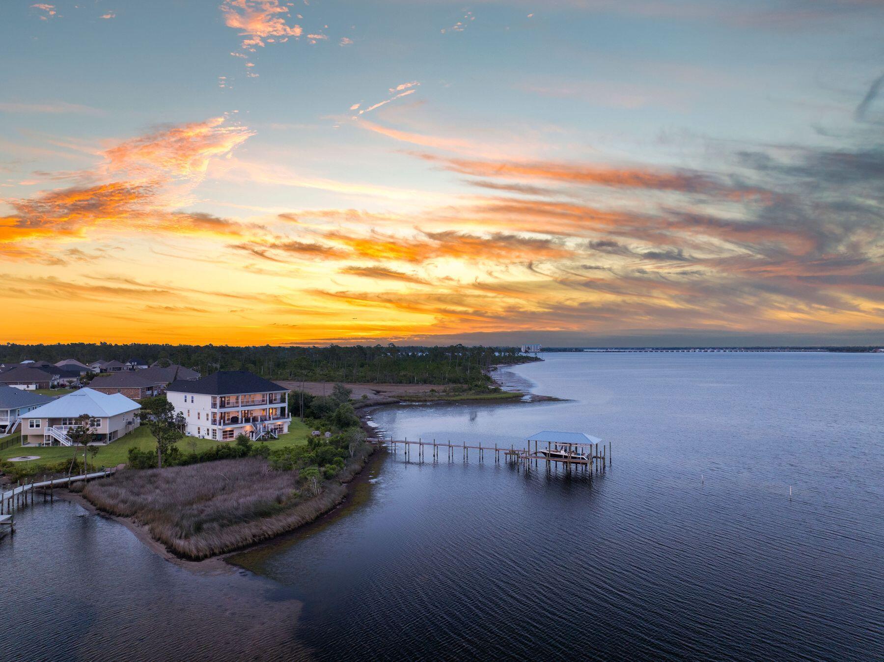 This custom-built waterfront retreat is more than a home; it's a private resort with panoramic bay views, a boat lift, and a show stopping game room unlike anything else. Presiding over North Bay, this home offers expansive living and soaring ceilings. This luxurious residence enjoys a quiet location set back from the street at the end of a cul-de-sac. Built in 2021, the home offers a magnificent game room/den complete with an island bar, dining area, pool table, and space for a home gym, tabletop games, and indoor ball sports. Multiple TVs provide the ultimate viewing for sports fans. Garage-style glass doors fully open to allow refreshing breezes indoors when dining on this level. As you approach the home, a broad staircase leads up to the main level. LVP flooring flows seamlessly through the open living space, formal dining area, and a spacious sitting room. Every seat has stunning views across the bay. A soaring volume ceiling with clerestory windows enhances the space and brings in an abundance of natural light. Gather around the gas fireplace after dinner and enjoy quality time with family and friends. The tall chimney wrapped in shiplap is the focal point of the living room. Lit by three pendant lights, the generous island announces the chef's kitchen, which is equipped with KitchenAid appliances, including a double oven. A pot filler is conveniently located above the smooth top range, ready for pasta nights. A walk-in pantry, laundry, and a wine bar make this the perfect home for entertaining. A wall of windows delivers sweeping bay views, which only get better when you step through the French doors onto the large covered composite deck. From the porch a staircase leads down to the manicured backyard. The primary suite is also on this floor and boasts a boutique-sized walk-in closet and beautiful bay views. The ensuite bathroom impresses with shiplap walls, a dual quartz-topped vanity, and a walk in shower wrapped with tile and glass. A neat makeup area completes this private haven. A guest bedroom, suitable for use as an office, and additional full bath completes the main level. Connected by a galleried walkway, the top floor comprises five additional bedrooms and two full bathrooms, as well as a bonus room. Doors open directly onto another full-width covered porch showing off the best views of the property. Where better to sip cocktails while toasting the sunset over the bay? The home features a two-car garage on the main level and an additional one and a half car garage on the lower level. A community pool offers more recreation beyond boating, fishing, kayaking, and paddle boarding from your private dock.