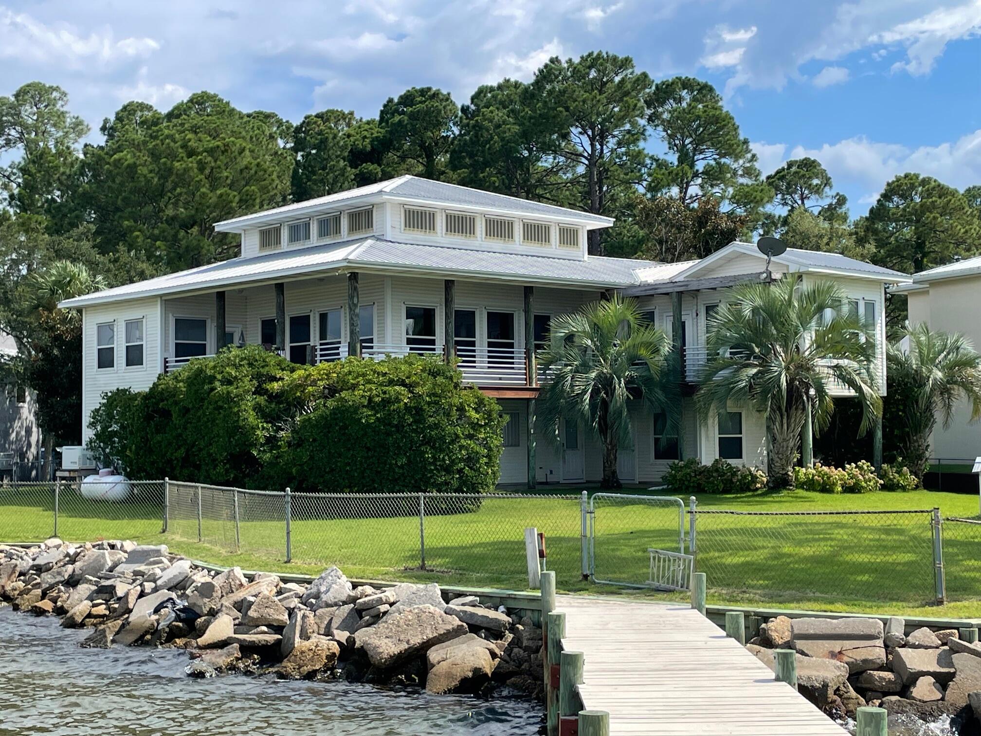 Live the dream in this spectacular Bay front oasis thoughtfully positioned on a rare double lot, where dazzling sunrises and sunsets light up the sky as dolphins occasionally glide past . Wraparound porches and patios offer breezy, shaded spaces to relax or entertain in true coastal style. The sun-filled main level features an open great room with panoramic views and access to a covered deck. An elevator makes daily living effortless. Private lower-level suite boasts a full kitchen/bath, spacious bedroom, and private patio--perfect for guests or extended family. A deep two-car garage with rear door offers ample storage for kayaks, paddle boards, or golf cart, plus workshop space. Private dock with two boat lifts and fish cleaning station for the catch of the day. Paradise awaits! Bay Circle has a dock with a covered boat lift with remote, walk around dock. There is also a second boat lift. This home also has an emergency generator.