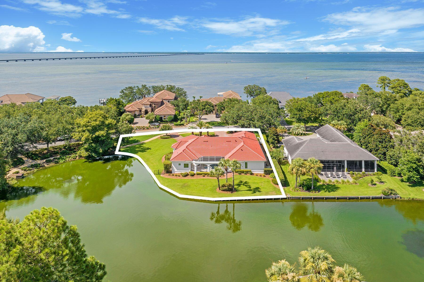Presiding over a lakefront lot of almost a half-acre, this magnificent Mediterranean-style home has many enviable features and updates. Beautifully architected on the outside, the home revels in its waterfront position with stunning views from most rooms in the house. The broad brick-paved driveway sweeps up to the three-car garage with ample space to accommodate cars and a golf cart. Shallow steps lead up to the imposing front entrance, with tall columns making a grand first impression. Leonardo travertine tile leads to the double door entrance, which opens into the first of two spacious living areas. Brazilian hardwood flooring graces each area, including the open chef's kitchen, which enjoys impressive views. Custom cabinetry, granite countertops, and stainless steel appliances make this a well-appointed space. Keen cooks will note the six-burner gas range/oven, dishwasher, wine cooler, and a pantry for storing additional items neatly out of sight. There's a breakfast bar as well as a dedicated breakfast nook for starting each day with the best views. Designed for entertaining, the kitchen opens into a family room with a fireplace, providing a cozy ambiance. This irregular-shaped room looks out directly onto the screened pool and spa, which in turn overlooks the peaceful lake. All on one level, the home flows through a series of dedicated spaces, including a sitting room, an executive study, a private sauna, and a laundry room. The formal dining room is illuminated by a breathtaking chandelier, making a grand statement all its own. Decorative tray ceilings with recessed lighting are bordered by elegant crown molding, while high ceilings and custom plantation shutters add a high-end finish. Three bright and airy bedrooms each have their own private bathroom, with a further half bath serving guests. The master suite outshines the rest with a sitting area for relaxing, a huge walk-in custom closet, and direct access to the lanai. The generous master bath features decorative lighting, a cultured marble shower, double vanities and a separate make-up area. The jetted tub is perfect for relaxing in this spa-like retreat, which includes a spacious dressing area. A new tile roof (2025), newer HVAC and water heater, and a recently resurfaced pool ensure many years of maintenance-free living. Tinted windows and three independently controlled zones for heat and air deliver the ultimate year-round comfort. Located in the premier non-rental community of Regatta Bay in Destin, this outstanding residence has the added assurance of gated security. High-end amenities include an 18-hole championship golf course, tennis courts, a gym, clubhouse, and a community pool. All this, just minutes from Destin Executive Airport, designer shopping, restaurants, fishing, and beautiful sandy beaches. Sold with golf cart.