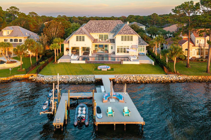 Bayfront living--elevated. Constructed with concrete and just 2 years young, this showpiece pairs resort-style amenities with a technology-forward, luxury interior and 112 feet of prime waterfront. Enjoy 7,020 sq ft of finished, heated/cooled space now, with an additional 2,955 sq ft pre-wired and plumbed for your ideal use and design.Inside, it's all about scale, light, and livability. Twelve-foot ceilings, 4'x2' tile throughout, double staircases crowned by chandeliers, and three sets of 9' sliding glass doors framing the bay. A chef's kitchen that actually cooks features Wolfe and Electrolux Commercial and touchless faucets. Entertain guests in your climate-controlled, glass-enclosed wine cellar capable of holding more than 1,000 bottles of wine. The primary suite brings hotel-level luxury with dual oversized closets and a 13'x7' spa shower (multiple shower heads, integrated speakers) and a free-standing tub. 
An oversized, storage-rich laundry room keeps life tidy. Whole-home conveniences include a central vacuum, security system with fire monitoring, full CCTV with motion detection, and a hidden concrete safe room with its own monitoring. Outdoor living is the headliner. A 1,435 sq ft 4-car garage anchors the motor court, while the covered summer kitchen brings the party: 42" commercial grill, commercial double burner, 60" Wolf hood with dual external vents, outdoor pizza oven (not built-in), 62" Arctic Air under-counter commercial refrigerator, NatureKast cabinetry, touchless faucet, wall-mounted Lava Aire fan/mister, Big Ass Fan, Hishizaki icemaker, and a 9'x4' island. Three remote screen enclosures open to a 50'x20' saltwater, ozone-filtered pool with water features, a 13'x16' spa with swim-in-place jet, commercial gas heater, two chillers, five in-pool barstools facing the bay, LED lighting, ten gas lanterns, a built-in fire pit, lounge seating (6 patio loungers + 2 pool loungers), two 70" outdoor TVs, Bose + Sonos audio, and a large storage room.
Your private waterfront playground. An oversized dock built with flow-through decking is specked for a future boat lift and includes a kayak deck, two 360-degree jet ski lifts, three ladder access points, perimeter uplighting, and full utilitiespower, water, internet, and camerasright on the dock. For added peace of mind, this home also features exterior perimeter security cameras, alarm system with fire monitoring, a solid concrete hidden safe room with CCTV camera systems, a cell tower, and a 48 KW Generac generator.

