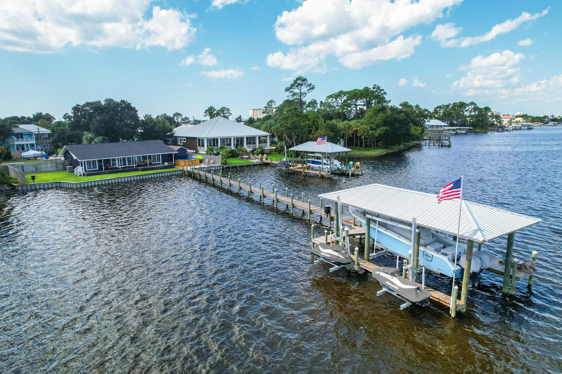 Experience unparalleled value in this stunning waterfront home, perfect for both boating enthusiasts and beach lovers. With over 100 feet of shoreline on the south side of Grand Lagoon, you'll find the sugary white beach just a few blocks away. This exceptional section of the lagoon is among its widest points and offers one of the quickest accesses to the open waters of the Gulf of Mexico. Plus, next door is one of the few remaining completely natural properties on the lagoon, ensuring your only neighbors to the east are the ducks and turtles. Unlike many boat-friendly homes in Panama City Beach, this residence is close enough to the beach to successfully rent short term if you would like to offset ownership costs. Despite the breathtaking views that make you feel like you are on a  private island, flood insurance is surprisingly affordable at just $3,166 currently. The interior has been almost completely remodeled since 2021, including the addition of a fourth bedroom clad in shiplap walls and ceiling. The kitchen boasts a spacious island, new cabinets and sleek quartz countertops. The living room ceiling has been raised and electric window shades were added. The master bathroom was fully redesigned with a beautiful tiled shower, a new double vanity, and shiplap walls and ceiling. The shiplap walls continue into the master bedroom, which has sweeping views of the lagoon and direct access to the back porch. Throughout the home, you'll find wood-look tile and LVP flooring. The living room and two of the bedrooms provide waterfront access to the back porch. Your new boathouse, dock, double jet ski lift, and seawall were completed in 2022. The boat lift is rated for 12,000 lbs and comfortably accommodates a 30-foot center console. The exterior features a new brick paver patio surrounding a 2024 swim spa with a bar upgrade that will convey, fresh exterior paint, new sod and irrigation system, hurricane shutters, impact glass sliding doors and windows, and almost 1,000 square feet of porches and decks overlooking the water. Around the corner from the swim spa, you will find an outdoor shower with hot and cold water and a detached workshop and storage building built with materials and paint that matches the home. The home is just a short drive or even shorter boat ride from local favorites like Captain Anderson's and Grand Marlin. For beach lovers, public beach access #9 is at the end of Biltmore Drive, while public beach access #11 just a bit to the west offers ample parking. The always popular Schooner's Beach Club is less than a mile away.