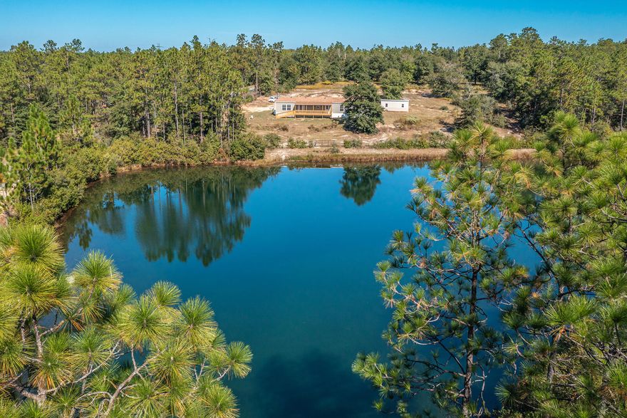 Modern 5 bed / 3 bath manufactured home on 3.71 acres of land, with tranquil view of a spring-fed lake! This home features an open and inviting floor plan. Spacious living room with cozy fireplace. The kitchen offers laminate countertops, gas stove, tile backsplash, and large island with breakfast bar.Primary bedroom with walk-in closet and a luxurious en-suite bath with double sink vanity, relaxing soaking tub, and separate shower.Split bedroom floor plan with 4 additional bedrooms and 2 bathrooms. Retreat outside to a large wooden deck with gorgeous views of the lake. The property line extends past the fenced-in area and includes two 20x20 horse shelters.Yard building to convey ''As Is''.