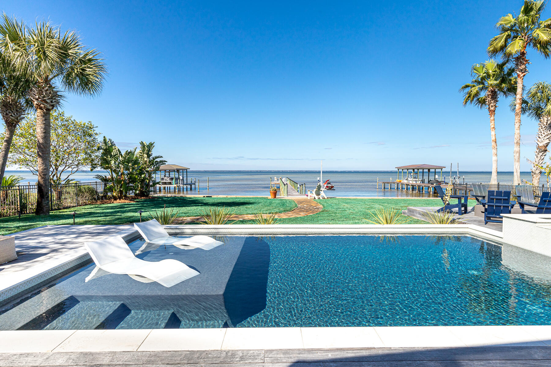 Sophisticated bayfront renovation and no HOA. Single-level living in a compelling floorplan that perfectly mingles privacy and invitations to gather. Curb appeal is unmistakable with a deep winding drive that leads to a pristine white home with a welcoming courtyard entry. Flexible design and a seamless floor plan endue an entertainer's enclave or a relaxed family estate. Sparkling bay views are first captured within the glass-paned front doors and then draw you in through the dramatic living area highlighted by a 12' coffered ceiling. An expanse of glass fully retracts, leading to a newly added screened-in porch and the bay beyond. A sprawling backyard is highlighted by a recently constructed heated pool and spa with a sunken fire pit.