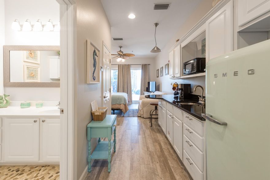 Bright Ground Floor Studio Near Pool and Beach. This bright studio is perfect for those looking for quaint luxury living. Very nice furnishings rest on gray and cream wood-look floors for a touch of rustic, and ivory walls with soft sage and pale aqua accents create a warm beach feel. Natural daylight streams into floor to ceiling glass with a sliding door to the covered patio. A bistro table and chairs set the stage for enjoying any meal outside, and a wicker love seat is perfect for reading or chatting with friends. Immaculate landscaping features brick pavers, walkways, tall palms and feathery shrubs.