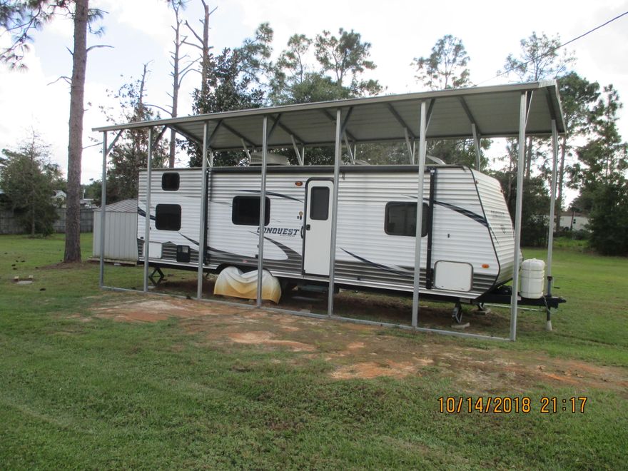 Nice camper on a cleared lot with a cover built over it.