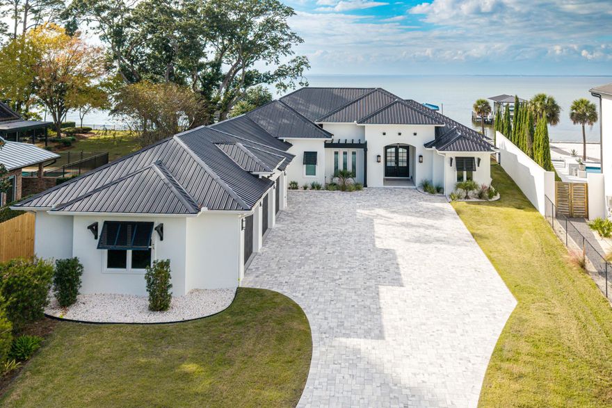 Experience unparalleled bayfront living in this 2022 custom-built estate, positioned on nearly one acre behind a private gated entrance. Designed entirely on one level with 10ft ceilings, this residence blends luxury with efficiency--featuring a rare 1,525 sq.ft. 4-car garage and a complete home solar system with bi-directional metering for low electric bills. Perfectly oriented to capture breathtaking sunsets over the western sky, this home offers resort-style outdoor living with a heated saltwater pool and spa, 800 sq.ft. covered lanai with full summer kitchen and Green Egg smoker, and 117 feet of pristine bay frontage complete with dock, swim platform, and boathouse accommodating up to a 30' vessel. Peace of mind comes standard with impact-rated storm windows and doors, metal roof and a whole-home generator. 
Inside, every finish has been carefully curated with whitewashed hardwood floors, quartz countertops, dual living spaces with a two-way gas fireplace, remote electric blinds, and Bluetooth fans. The entertainer's kitchen boasts a double oven gas range, expansive center island, large walk-in pantry, and bayfront dining nook with built-in seating.

The waterfront primary retreat offers its own private covered porch and a spa-worthy ensuite with dual vanities, walk-in shower, soaking tub, and dual walk-in closets.

Sunset serenity, luxury craftsmanship, and energy-efficient living - all in one extraordinary bayfront estate.

Enjoy a community park equipped with a playground, tennis courts, picnic tables and more. Driftwood Estates is conveniently located near Sacred Heart Hospital, Publix, fabulous dining and shopping in Grand Blvd, and just a short drive to the beaches of 30A.
