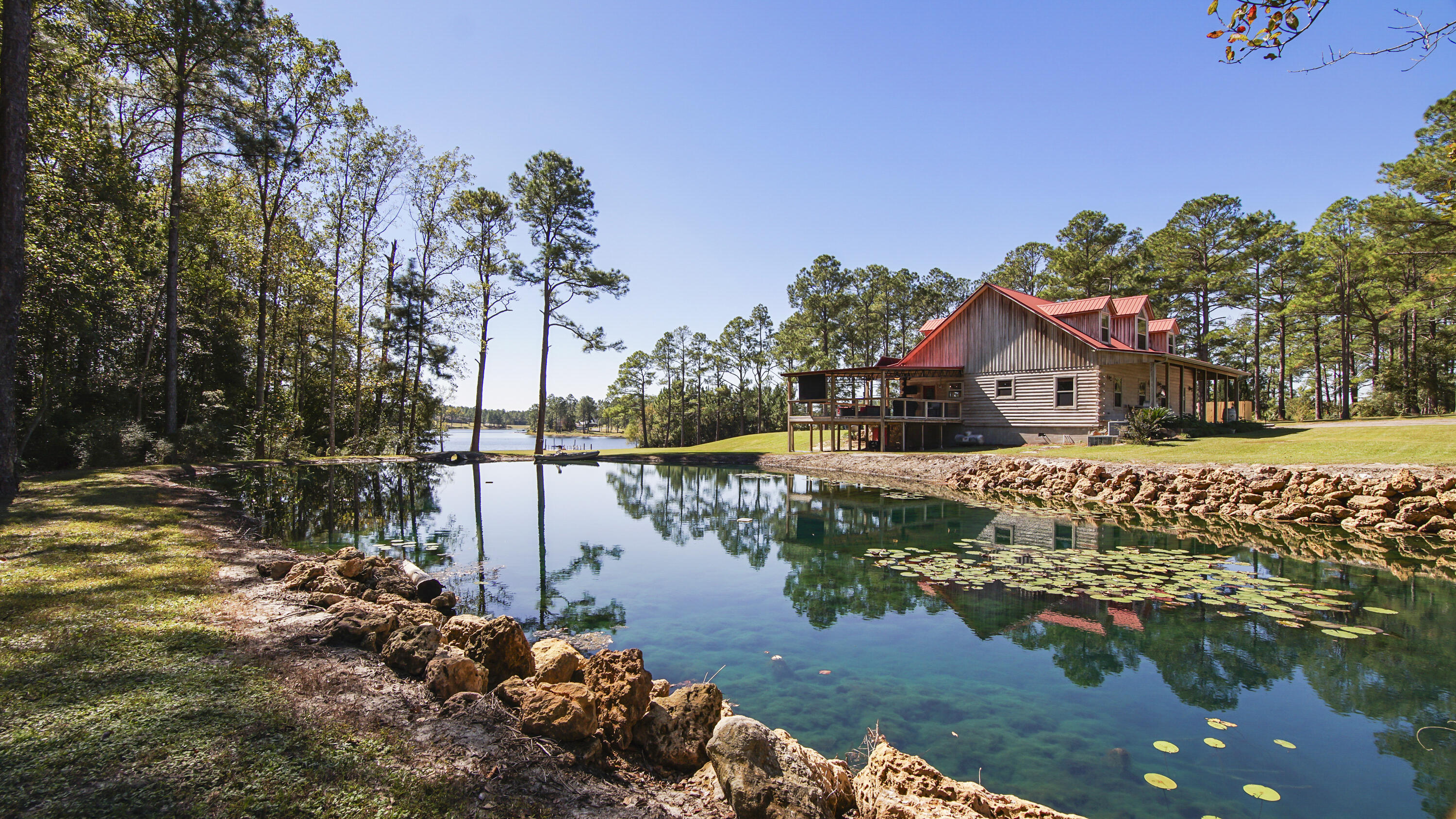 Discover this stunning 2,883 SF log cabin-style home, nestled on 4 spectacular waterfront acres with nearly 300 feet of lake frontage, plus a private pond, offering the best of both worlds. This cypress sided 5-bedroom, 3.5-bath retreat, formerly a contractor's personally built home, features innumerable distinctive features, setting it apart from the ordinary, and has no HOA! The home features over 1,000 SF of inviting porches, perfect for taking in both the sunrise and sunset. Each room maximizes calm water views with walls of windows, bringing in loads of light. The spacious family room highlights its soaring pine cathedral ceilings & overhead loft and walkway, while overlooking the lake. All the work has been done and it is truly move-in ready with fresh paint and new flooring throughout much of the home. The kitchen sings with exquisite details: apron-front hammered copper farm sink with 2nd bar sink in the island, wine fridge, double wall ovens, gas cooktop, stained glass details and even a life-size chalkboard and built-in desk with bookshelves for homework, cookbooks, etc. The pantry is so expansive, it's like having your own personal general store! Adjacent is the captivating dining room, complete with custom black tin ceiling & oak ceiling medallion with stained glass chandelier. The downstairs master bedroom has stunning lakefront views, a window seat to enjoy them, and an expansive walk through closet (& dressing area complete with separate vanities) thru to the luxurious master bath. Enjoy soaking in the jetted tub and separate 4x8 tiled shower with two shower heads. The remaining 4 bedrooms are upstairs, each designed identically. They each have an additional super cozy loft area for kids, designed especially for a twin mattress, accessed by ladder (or just use it for storage!). A few special details are: wrought iron railings, pine ceilings and wainscoting and 2'' wood blinds. This home is unmistakably designed for entertaining and gathering together, both indoors and out. Step outside to your very own massive party deck overlooking the pond and the lake on your giant 24x24 deck, just off the kitchen; perfectly laid out for cookouts - or the addition of a hot tub! Picture friends and family watching movies or celebrating game days on the deck, as it comes fully equipped with a pull-down screen for outdoor viewing.
Whether you're fishing or just relaxing, you'll not only enjoy the floating dock, you can "put in" right from your back yard with a private boat launch. As a bonus, the property includes a 1,000+ SF shop with water, electricity, an automatic garage door, with ample storage, including overhead loft storage. A perfect place to tinker or store your holiday decorations. An oversized, extra tall carport with a RV hookup, provides a convenient spot for your RV or additional vehicles. There's even a lighted basketball court on the grounds.
Be sure to click on the photos to see a list of features like 2x6 walls along with survey and the floor plan.
Best of all, this incredible property comes with no HOA restrictions, offering you the freedom to truly make it your own. With almost 300 feet of prime waterfront, this lakeside log cabin is the perfect blend of tranquility, space, and adventurewhether you're seeking a peaceful retreat or an entertainer's dream! This would make a superior corporate retreat, short term rental, or of course, a personal home (and to date, it has always served as a family home). What this property embodies is in the very name itself: HAVEN. 
