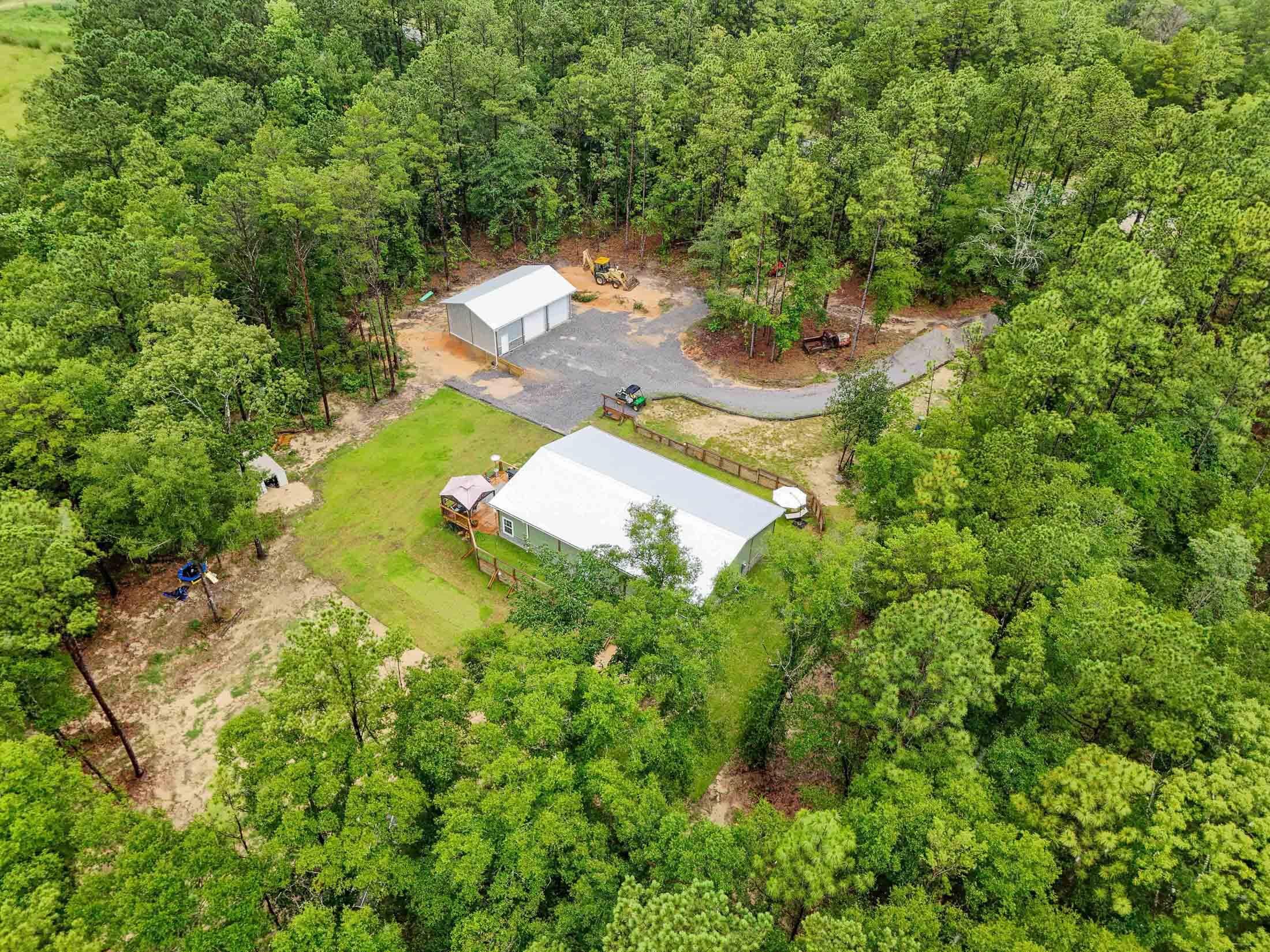 Experience the ultimate in country living with this 2-year new, captivating 3-bed/2-bath barndominium, a contemporary take on rustic living. Situated on 6.3 acres, this home is a hidden gem, nestled in a clearing, tucked away from the road, accessible by a picturesque winding drive. The expansive great room, with its tongue and groove vaulted ceiling and engineered bamboo flooring. warmly invites you inside. You'll never miss a moment in the kitchen with friends and family again with this open plan. Every inch of this home exudes charm, from the craftsman-style kitchen cabinets to the custom island. The kitchen features stainless steel appliances, a custom range hood, and a sizable walk-in pantry. The bedrooms - in fact all rooms - are large, with 9' ceilings and lots of