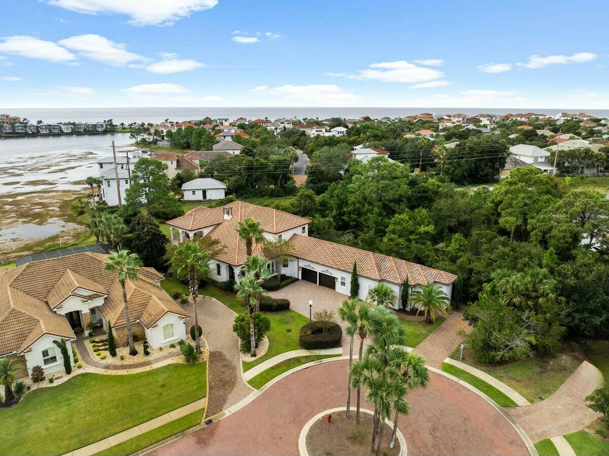 This outstanding lakefront property presides over a half-acre lot featuring well-tended landscaping and space for a pool. The exceptional quality and architectural sophistication put this Destiny East home in a league of its own. Two living rooms, one on each level, provide comfortable living spaces for larger parties. Luxurious furnishings, wood flooring and a corner fireplace create an inviting ambiance beneath the deep trey ceiling. The gourmet kitchen is an entertainer's dream, with high-end appliances, a granite-topped island and tons of storage in the dark wood cabinetry. Casual dining can be enjoyed at the breakfast bar, and guests will appreciate mesmerizing bay views from the more formal dining area. For outdoor dining, sliding glass doors open onto the covered patio with an outdoor kitchen, built-in grill and beverage refrigerator. The slate-tile flooring provides ample space to relax and enjoy the idyllic view framed by elegant arches. Head up the grand staircase and onto the second-floor balcony to fully appreciate the serene lake views. Six spacious bedrooms and five full baths can accommodate up to 22 guests. Young visitors will appreciate the bunk room, wet bar and the game table on the landing. The primary suite has a lavishly appointed bathroom with his-and-hers vanities, a whirlpool tub and a walk-in shower. Of the six bedrooms, three of them are considered master suites (two of which are in the main house and the third being in the guest quarters). All provide ample space and privacy. A separate guest suite boasts its own independent access. It's fully appointed for longer stays with a private living area, wet bar, kitchen, bedroom and bathroom. The sweeping paved driveway and a two-car garage take care of multiple vehicles. This high-end gated community has a neighborhood pool, hot tub, tennis courts, playground, a community room for movie nights and a well-equipped fitness center. The nearest public beach access is next to the Crab Trap and offers miles of soft white sand and emerald gulf waters. Other amenities nearby include Whole Foods and Publix, Big Kahuna's Water Park, Destin Harbor, shopping at Destin Commons and a wide choice of world-class golf courses.