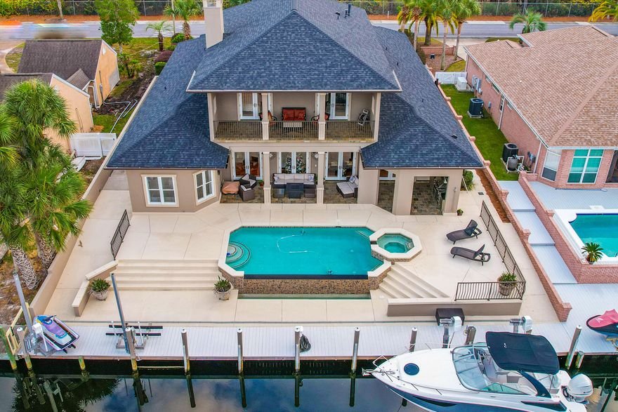 JUST REDUCED!!! Mesmerizing CANAL FRONT home featuring a Heated Infinity Pool w/Hot Tub, Whole Home Generator, Boat Dock/Lift with 2 Jet Ski Lifts, Seawall, Outdoor Kitchen, and Minutes to the Beautiful Gulf-of-Mexico. From the time you enter the grand foyer you can feel the space this open concept home has. The living room is straight ahead featuring river bottom pinewood floors that are outlined with travertine, gorgeous stone gas fireplace, and triple French doors overlooking the pool and canal. To the immediate right is a bonus room, which could be used as a 4th master suite with beautiful custom windows allowing for natural lighting and features a wet bar with an ice maker. The dining room is to the immediate left with custom arches and a stunning chandelier with matching scones.