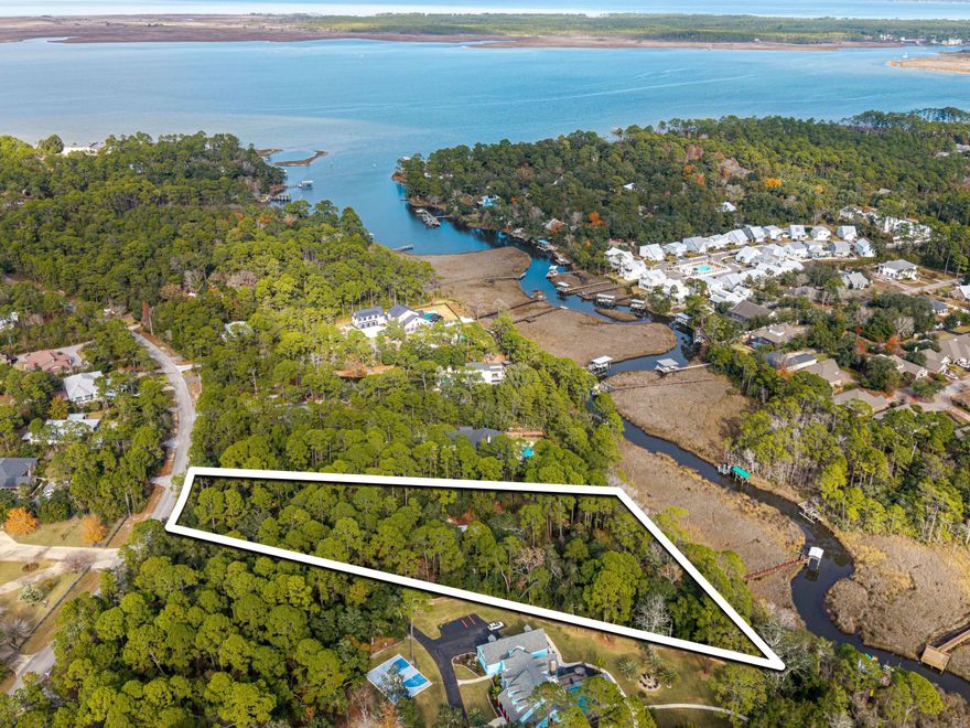 Set along the quiet curves of Turtle Creek, this rare waterfront offering unfolds across nearly three acres of wooded privacy, with approximately 270 feet of frontage on a deep-water stream. Towering mature trees frame the setting, creating a park-like environment that feels timeless and secluded while offering direct access by boat to Hogtown Bayou and Choctawhatchee Bay. With a dock and boathouse already in place, the property invites a lifestyle shaped by calm mornings on the water and effortless year-round navigation. The existing residence is a custom-built carriage house finished in classic brick and Hardie siding. Elevated living defines the second floor, where reclaimed barn-wood floors ground the main living area and the primary suite in warmth and character. From this vantage point, the home feels suspended among the trees, offering a peaceful, treehouse-like perspective with leafy views in every direction. The layout was thoughtfully designed to support future expansion, originally envisioned as a guest house once a primary residence is constructed on the property. On the ground level, the heated and cooled garage has been converted into additional living space with bedrooms, laundry, and a secondary living area. This space was intentionally built so it can be easily returned to garage use once a larger home is completed, preserving flexibility for future plans. Two additional structures expand the possibilities. A 12-by-36-foot building includes 240 square feet of finished, climate-controlled space currently used as a casual retreat, with the remaining area dedicated to storage. A fully enclosed pole barn measuring 24 by 36 feet offers ample room for equipment, vehicles, or workshop needs. Seller-held plans allow for the option to significantly expand the existing structure by doubling the heated and cooled square footage and adding 810 square feet of covered parking. The property is offered as-is, with the seller willing to manage the proposed addition for a fee, creating a rare opportunity to shape a legacy waterfront estate while enjoying immediate use of the property and its natural surroundings.