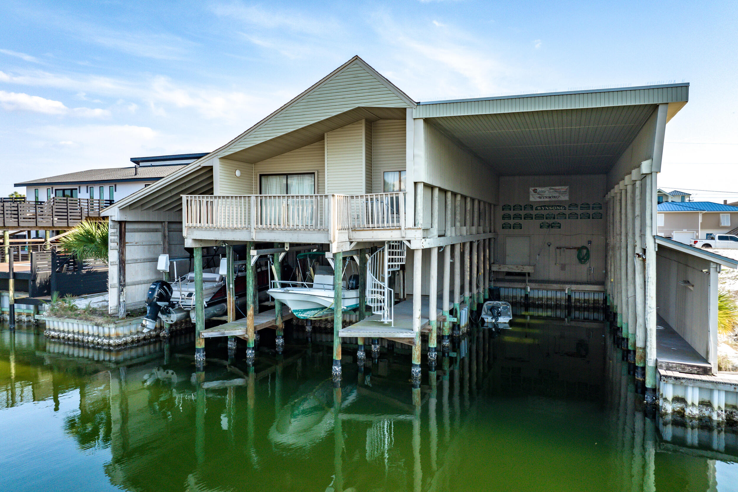 607 Magnolia Drive is a canal-front, two-bedroom, two-bath combination house/multiple covered boat slips, located on Holiday Isle. This is one of the most unique boathouses you'll find in Destin! Below the main house, you will find an unusually large assemblage of three semi-enclosed boat slips, a tackle room, and a garage. The largest slip can accommodate a 60-ft. boat, and the two smaller slips each have their own boat lifts. The main house has an open floor plan. It has a vaulted ceiling in the living/dining room, and a kitchen with a breakfast bar. From the living room, there is alternate access to the boat slips through the balcony and via a spiral stairway. The tackle room contains the washer and dryer and a water closet. The lot provides 90 feet of canal frontage. With a unique network of canals, Holiday Isle (often referred to as Norriego Point) is a sought-after peninsula, located between the Gulf of America and the Destin Harbor - providing easy boating access to the Gulf, the Harbor, East Pass, Crab Island, and Choctawhatchee Bay.