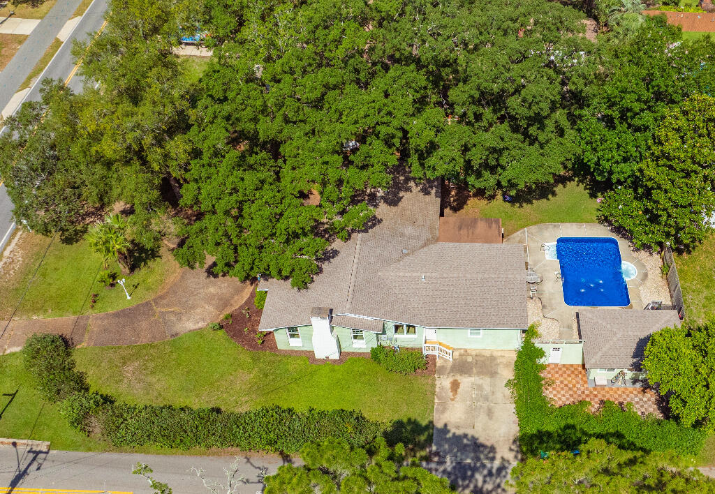 Move-in ready and full of charm, this historic Gulf Breeze Proper pool home was built in 1955 by the Berry family. It features original hardwood floors, quality craftsmanship, and a spacious 2016 Master Suite addition. The den impresses with a large stone fireplace, wainscoting, built-ins, and an 85' TV that conveys. Outdoor highlights include mature landscaping, a pool with new liner, bamboo Zen garden, and the original 'Summer Kitchen'--a 300 sq ft outbuilding with A/C. Impact features provide low insurance costs. Located in Flood Zone X, this off-grade home blends history, comfort, and modern updates.