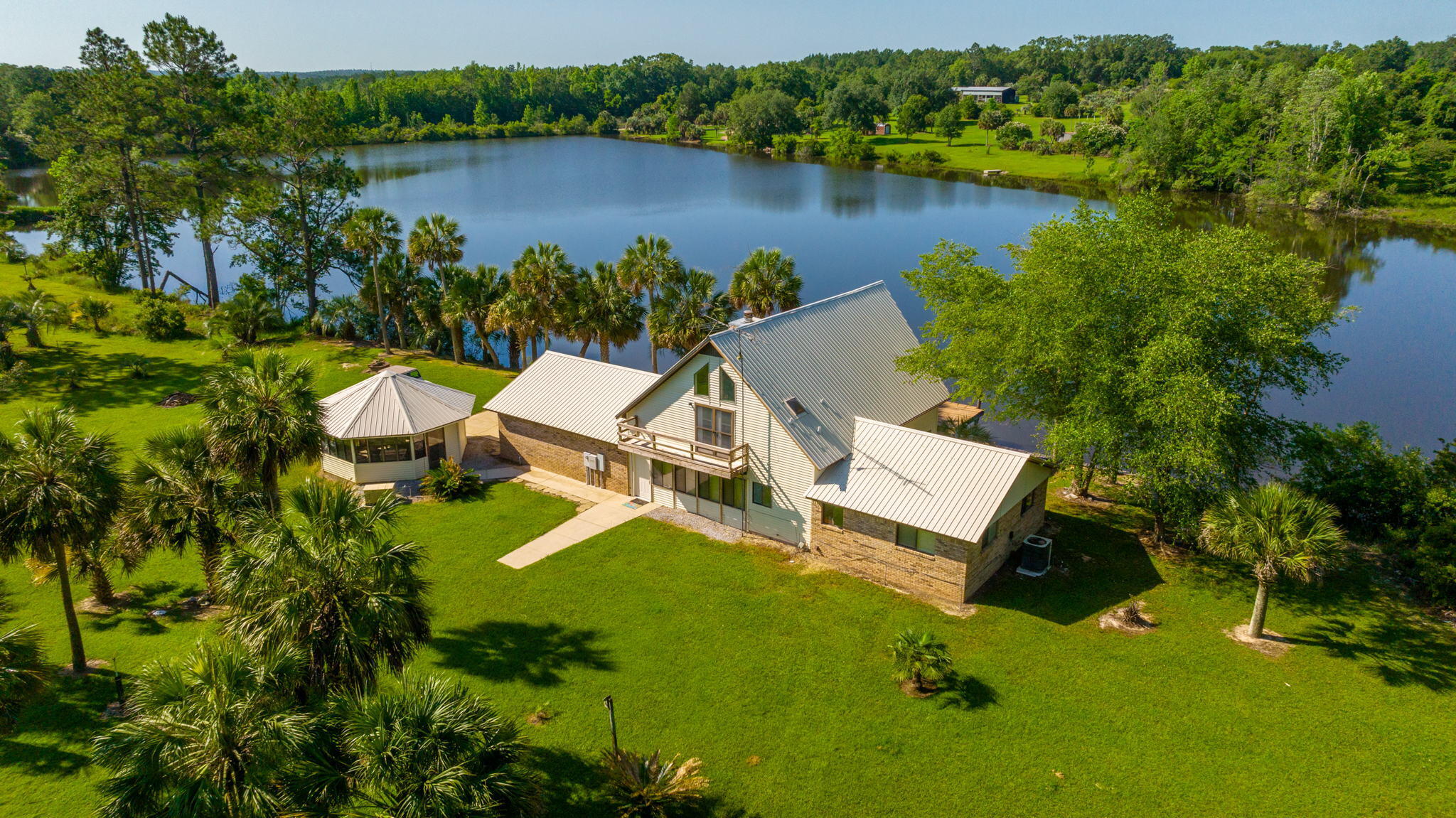 Country Waterfront Estate!!! Enjoy panoramic views and beautiful sunrises/sunsets over the lake from your home or dock! A truly unique property w/ a large amount of water frontage and approximately 20 acres. The property is mostly wooded but partially cleared where the home site is located... The cleared area has lush green grass and is scattered about with mature palm trees. The home is a unique design and features a large living room, galley kitchen w/ breakfast bar and 2 bedrooms/1 bath downstairs. Upstairs is a loft area that overlooks the downstairs living room and is used as a 3rd bedroom. A full bathroom is also located upstairs. The home has a 2 car garage and gazebo located to one side that is screened-in and great for entertaining guests. Buyer to verify all areas of importance.