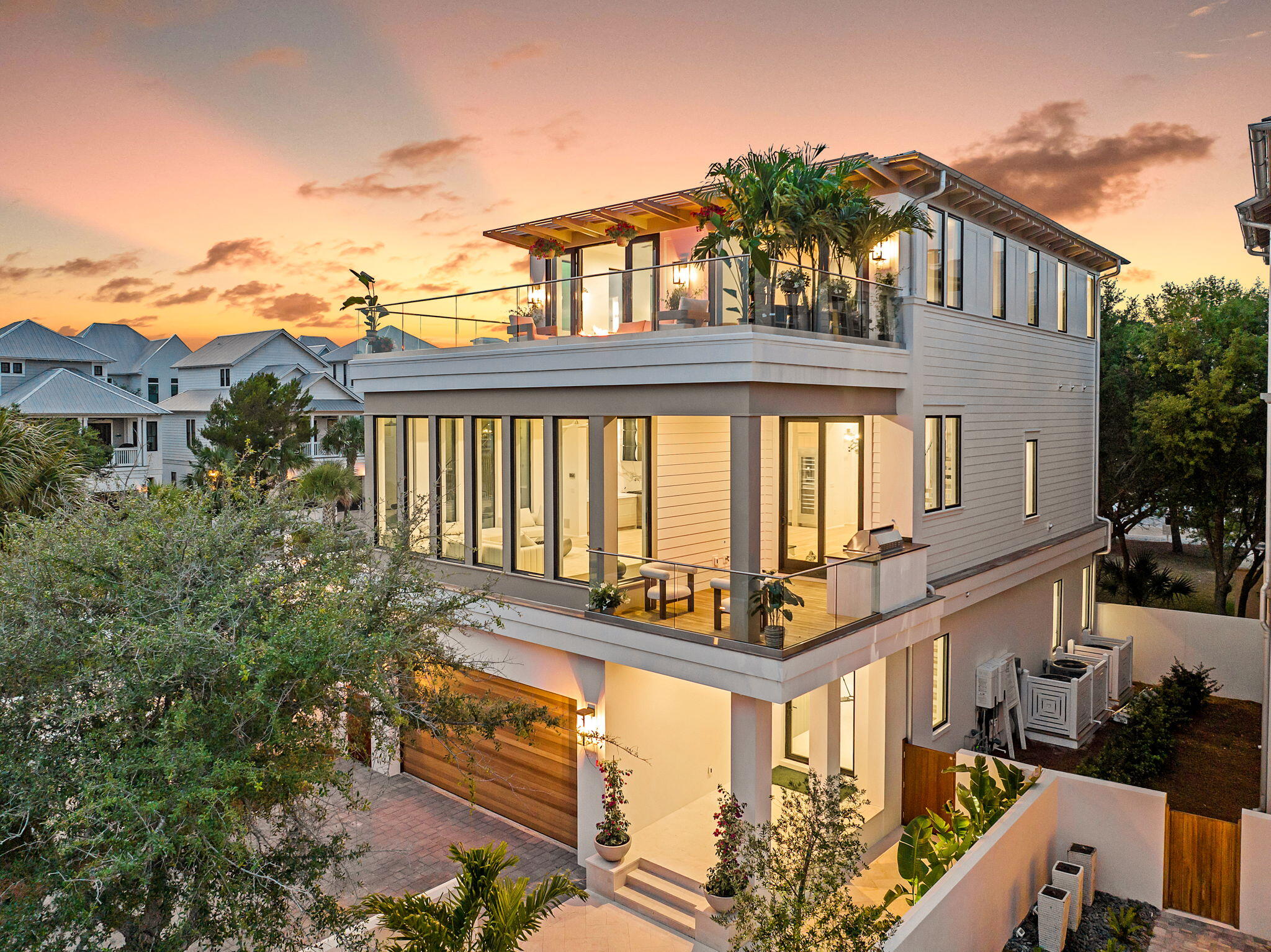 The Glass House is a striking new architectural statement in Seagrove Beach, completed in May 2025 within the private gates of Seanest Village. Designed by Gregory Jazayeri of GDJ Design and Ivana Jazayeri of IVA Design, and built by Lpkk, Petr Kasparek, this 3,967 square foot residence offers a rare balance of timeless craftsmanship and modern innovation, equally suited for refined vacation living or full-time residency. Built with concrete block construction on the first floor, the three-story home features five bedrooms, five and a half baths, and three spacious living areas, including double primary suites thoughtfully designed for flexibility and comfort. Ceiling heights soar with 10 feet on the first and third floors and nearly 12 feet on the main living level, culminating in a large rooftop terrace where Gulf views stretch beyond the treetops.
Inside, a state-of-the-art technology suite complements sleek custom finishes. An 85 inch display anchors the audio-visual system with immersive surround sound, whole-home WiFi, Alexa integration, and exterior security cameras. Custom white oak cabinetry, Thermador and Viking appliances, Kohler fixtures, and smart bidet toilets reflect an uncompromising standard of modern luxury. Offered furnished, the interiors blend clean lines with curated modern pieces, creating a ready-to-enjoy coastal retreat.
The first floor is anchored by a glass pivot door entry, leading to a guest suite, bunkroom with custom queen over twin bunks, two full baths, a lounge with wet bar, and shaded porch opening directly to the Seanest pool and boardwalk.
On the second level, walls of glass frame the shimmering pool while a peninsula fireplace connects the living, dining, and kitchen spaces. Culinary features include a chef's kitchen with Thermador appliances, a 48 inch Viking gas range, hidden oversized butler's pantry, and a 66 bottle glass wine display. A junior primary suite, laundry, powder room, and outdoor grilling porch complete this floor.
The third floor offers Gulf facing vistas from a morning bar and lounge, alongside the primary suite, a serene retreat with a glass display walk-in closet and spa-inspired bath featuring a freestanding tub, dual vanities, and a double shower. A second laundry space and an additional bedroom with bath nestled beneath the live oaks round out the level.
Residents of Seanest Village enjoy two vanishing edge pools, deeded beach access, and direct entry to the neighboring State Forest, all within walking distance of dining, shopping, and the new Greenway Station.