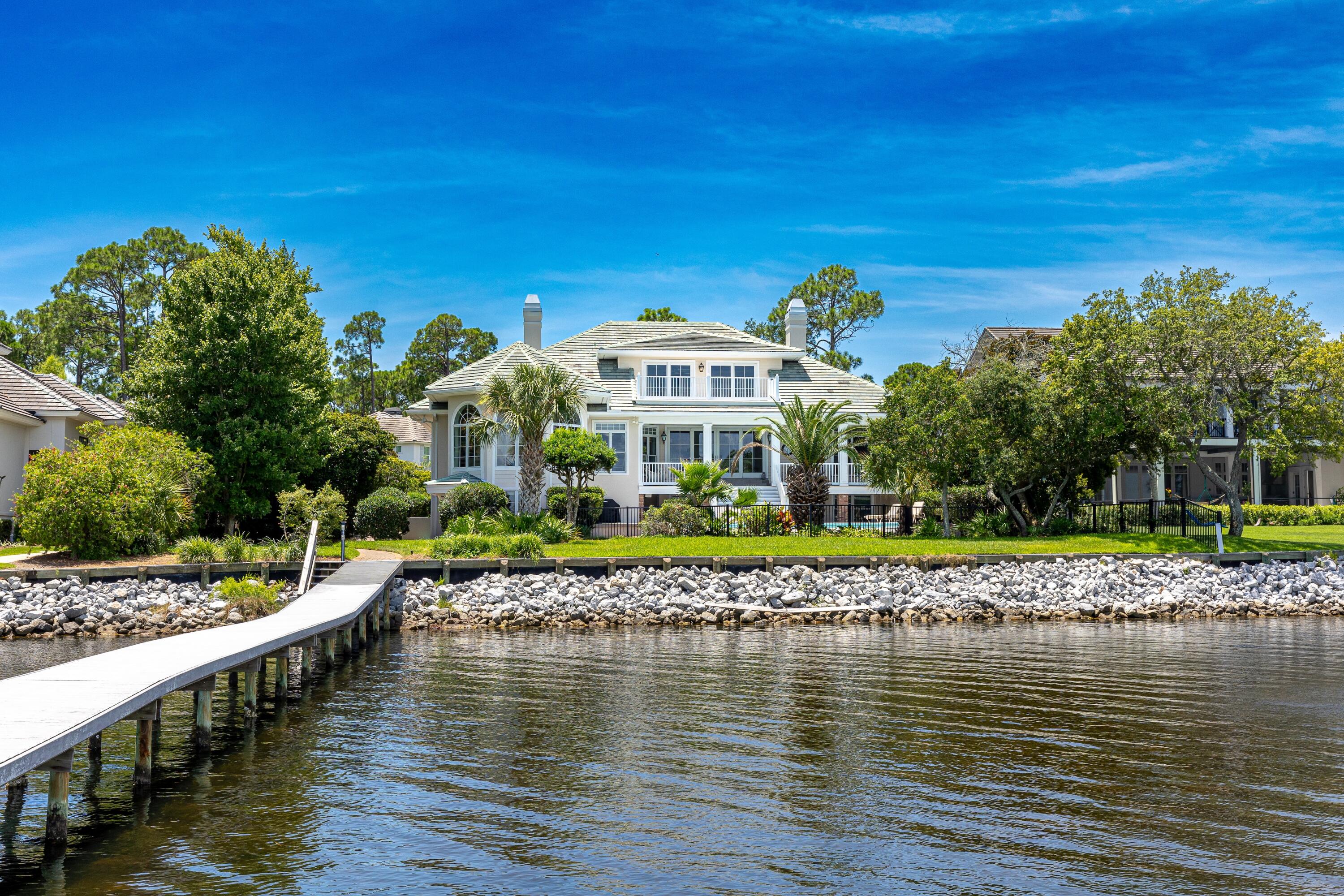 Timeless elegance on the bay behind the gates of prestigious Regatta Bay Golf and Yacht Club. This enchanting sanctuary sits surrounded by lush, mature landscaping, perched over 108' of water frontage with endless bay views. Remarkable in detail with deep porches and graceful design, it exudes a sense of grandeur while embracing impeccable craftsmanship and tranquil comfort. Reminiscent of Louisiana low-country homes, Prescott Architects' raised design highlights water vistas from every vantage point. A rare combination of warmth and space, it measures over 6000 square feet in heated space with over 1000 square feet of porches. Enter a commanding facade to a grand entry which reveals impeccable inlaid marble flooring joined by immaculate hardwoods. Substantial 10" layered crown molding, and 10' high ceilings complete the space. Arched, paned windows frame memorable sunsets and further enhance the remarkable design. Living, dining, and sunlit parlor flow seamlessly and serve as family's central gathering space and an entertainer's delight. The gourmet kitchen with prep island, serving bar, and breakfast area, boasts all white cabinetry, a separate wet-bar, Sub-Zero refrigerator, Viking gas range, and enjoys its own water views. An elevator conveniently services two of the homes floors and is flanked by a private powder room and additional storage. The main floor includes a bay front primary bedroom suite with its own cozy fireplace, dual vanity bath and a free-standing brass accented soaking tub with separate shower. The main floor is completed by a formal dining room and two additional bedrooms with a shared connected bath. Stroll upstairs for fun and games. The recreation room/library leads to its own private balcony through sliding full-wall glass doors. Spacious enough for a pool table and a crowd, it serves as the party spot but is secluded enough for a reading room. A full bath and heated and cooled storage area completes the space. First floor, a highly sought after and secluded guest suite with a kitchenette and private entry provides quiet and comfort for guests or extended family members.  A full bath is attached to this suite, which also leads to the pool area. Downstairs is complete with laundry, two additional bedrooms and another full bath. The infinity pool and hot tub are classic in lines and timeless in detail. Recently redecked and measuring 30'X18', it plays a central role in the home's fun and allure. Mature landscaping leads to a seawall and to an extra long 160' dock with covered boat lift. The 3-car garage affords extensive space for vehicles and storage needs. This exceptional estate offers a lifestyle of grandeur in which every detail has been thoughtfully considered to create a haven of comfort and tranquility. Experience the enchantment where refined living meets natural beauty and indulge in an extraordinary retreat. Regatta Bay is a guard gated community boasting the Regatta Bay championship golf course, including the clubhouse and restaurant, tennis and pickle ball courts, and a community pool. A golf cart ride to the Legendary Marina and Yacht Club, Lulu's bayside restaurant, and the area's best shopping and dining, including Whole Foods and Destin Commons, it is Destin's most convenient location.  