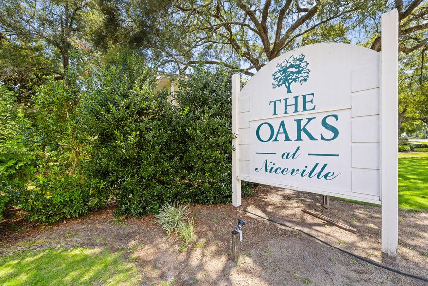 A charming furnished first-floor oasis is waiting for you to discover the low-maintenance and well-maintained unit tucked at the rear of building #13. Imagine stepping off your private porch while the summer breeze rustles through mature Leland Cypress needles.  As you cross the threshold of the front door, the 9-foot ceilings and soft planks of new vinyl flooring welcome you home. Sunlight filters past neutral-hued walls and faux blinds, casting a gentle glow on the sleek white kitchen where the aroma of fresh coffee drifts from a cup perched beside the glass-top stove. In the mornings, you can linger over breakfast in the dining area. Late afternoons are spent lounging poolside with neighbors you've come to know by name. Evenings are spent relaxing in the living room, (click 'more') where there is a dedicated alcove designed for your big-screen TV. Nights find you curled up in your master haven, doors closed against the world, surrounded by garments curated in your walk-in closet. This isn't just a condo - it's where your next chapter in life begins. Both bedrooms boast ceiling fans, faux blinds, and window sheers, 6-panel interior doors. The master offers a walk-in closet with extra hanging poles perfect for the fashion-forward homeowner. The guest room has added shelving for storage or additional organization. The hallway features a utility closet and the laundry closet that is equipped with a stackable washer and dryer, making laundry day a breeze. The Oaks community amenities include an in-ground swimming pool, multiple gazebos, bicycle racks, BBQ grills, and lush landscaping. Everything you need is included - just bring your suitcase and settle in. Oh, did I mention that the middle school, high school, children's park, library, and more are located within just a few short minutes of this community? 

