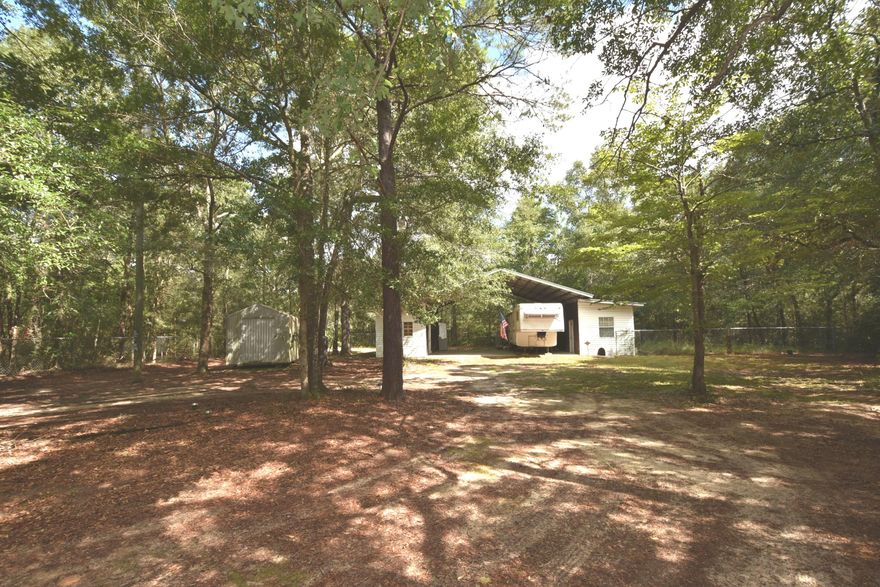 10 acres of beautifully wooded level land...a  pole barn covering for an RV w/2 side rooms and 2 storage buildings...located on a paved road...all for just $85K! Private drive through the front 5 acres takes you to the RVPort  located on the back 5 acres. Most of the back 5 acres is the wooded land behind the RV-look at the aerial included in the pictures. The fenced area around the RV site is not representative of any property lines. Once you purchase the property, you may be able to sell either half as they are separate parcels; check with county growth management. Utilities are in place but seller makes no representations and all improvements are conveying ''AS IS'. Septic tank is-'AS IS'.  RV may be removed from the property.