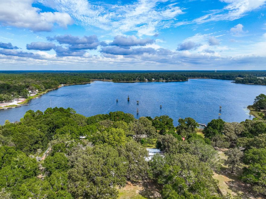 Rare opportunity to own a LAKESIDE RETREAT  nearly 2 acres of fully fenced waterfront property on Lake Holley, a 400-acre fishing lake known for trophy bass, bream, and bluegill. This two-story home offers a functional layout with a fully updated kitchen, tile flooring throughout the main level, and hardwood stairs leading to two spacious upstairs bedrooms. The main-floor primary suite provides convenient single-level living, and large windows offer peaceful lake views and natural light. A screened-in back porch overlooks the water, while the private dock is ideal for fishing, kayaking, or simply enjoying the sunset. A detached structure--formerly a she-shed and now accessed by a sidewalk--offers excellent potential as a lock-out guest suite, artist studio, or a short or long-term rental. Multiple outbuildings and covered carports offer storage, workshop potential, and parking for RVs or extra vehicles. With no HOA and endless flexibility, this property is perfect as a full-time residence, weekend getaway, or investment opportunity just minutes from DeFuniak Springs.