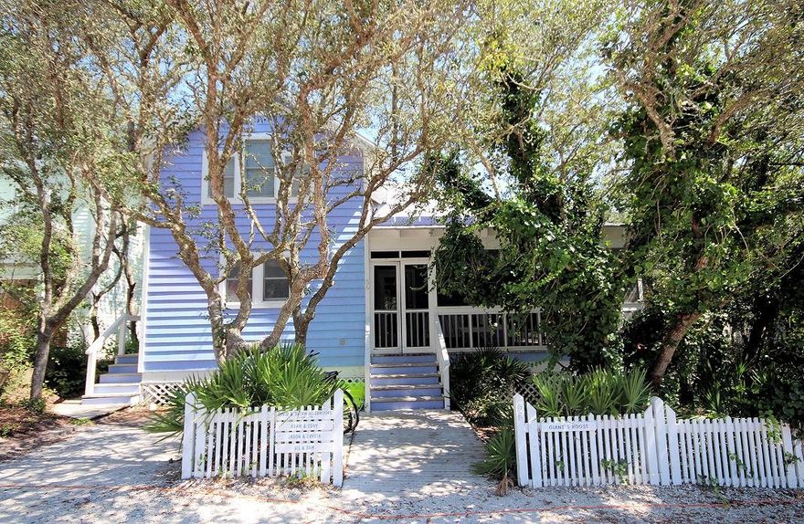 Located within the first block in Seaside on Tupelo Street, this Seaside cottage along with its guest house is located on a large lot with room to expand. The main cottage is surrounded by a grove of shady oak trees and has a generous wraparound porch. A glass top table with a collection of sea shells and sugar white sand from the beach underneath is the perfect spot for lunch or playing your favorite board games. Adirondack chairs and porch swing are just around the corner to sit and relax. White washed wood walls and pine floors were used throughout the interior. The living and dining area feature a double height ceiling. Galley kitchen off the dining area is separated by a breakfast bar. First level includes a half bath with access to outside shower.