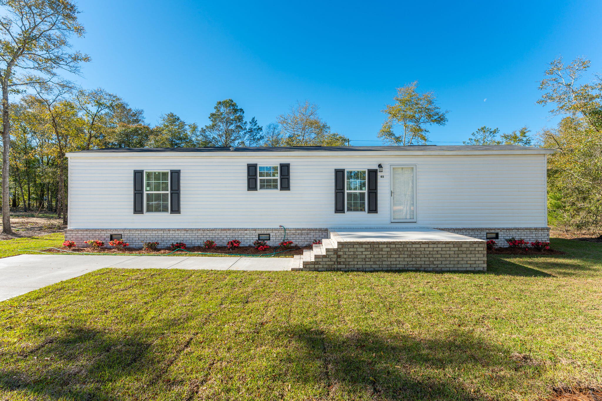 This charming 2-bedroom, 2-bathroom manufactured home has many upgrades from your standard build. The walls in the home are complete with sheetrock throughout and you will love the look that the wood trim and baseboards add. The linoleum flooring runs throughout giving a seamless view as you walk through the home. Both bathrooms have been upgraded to add ceramic sinks. The Kitchen includes a cozy dinette area for a small dining table. There is a walk-through utility room that includes the washer/dryer hook-ups, and this area leads out to the back deck that looks out over the beautifully sodded back yard. For some added energy efficiency, the HVAC unit is a heat pump system and rather than the standard manufactured home skirting, this home has brick underpin, helping to protect the underbelly of the home while adding more curb appeal for a nice look. What makes it even better? The concrete parking pad and sidewalk up to the concrete/brick front porch for a cleaner entrance into the home.
This adorable home is ready for its new owner. Come see it today! Located just about mid-way between Crestview and DeFuniak Springs, with less than an hour drive to the beautiful white sandy beaches of the Emerald Coast! (Agents please schedule showings through ShowingTime)