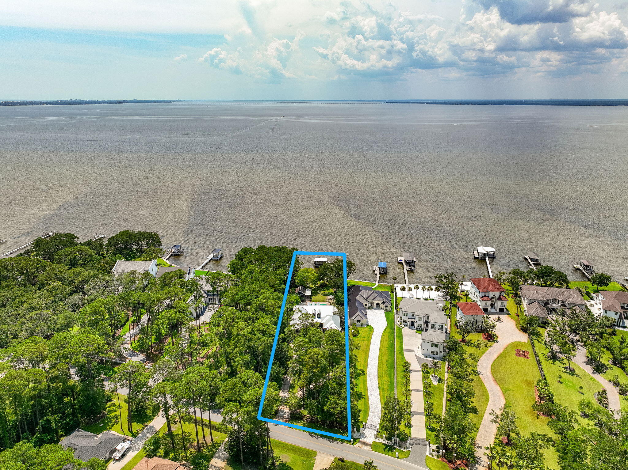 Watch the sun sink into the bay from this custom-designed, majestic waterfront estate on a sprawling 1.1 acres with dockage, spacious pool and plenty of room for indoor and outdoor entertaining. From the long circular drive to the charming central courtyard ringed with balconies, this 7,401 sf home embraces your family and friends with the warm and welcoming spirit of New Orleans. While space abounds, the 7 bed/5 full bath/2 half bath compound is comfortably divided into a two-wing main home, separate carriage house with an efficiency apartment, expansive pool deck with brick fire pit, and a fun summer kitchen/man cave with the cozy atmosphere of a local bar and grill. The main home wows your guests with a dramatic front entrance, antique doors, copper gutters and stunning old Chicago brick accents while old-fashioned Southern charm invites them to stay with brick interior archways, outdoor alcoves for reading or relaxing, plus private covered balconies and porches tucked in throughout the design. The main house gourmet kitchen is outfitted with a new Subzero refrigerator, two Bosch dishwashers, Jenn-Aire cooktop, wine coolers, warming drawer and an oversized L-shaped granite island. The adjoining dining room includes the convenience of a built-in custom buffet with warming drawer. The primary bedroom is on the ground floor with open bay views, soaring ceiling, separate sitting area and a stunning primary bath with a surprise private garden. Upstairs are two more bedrooms and full baths, and a recently updated media room/gym/bonus room.
The separate two story guest wing adds 3 more bedrooms, 2 full baths and a separate full kitchen. The estate also offers the advantage of two laundry areas.
Outside is a substantial backyard and a huge 20 x 40 pool trimmed in Tennessee bluestone. The bayfront dock includes two boat lifts, a boat house, jet ski lift, kayak platform and flow-through decking for longevity. The main house and guest annex also have a new metal roof. Driftwood Estates is located down Mack Bayou near Sacred Heart Hospital, A+ rated public schools, Grand Boulevard for dining and shopping, and is just minutes from 30A beaches. Call today to schedule your private visit to this one-of-a-kind estate.
