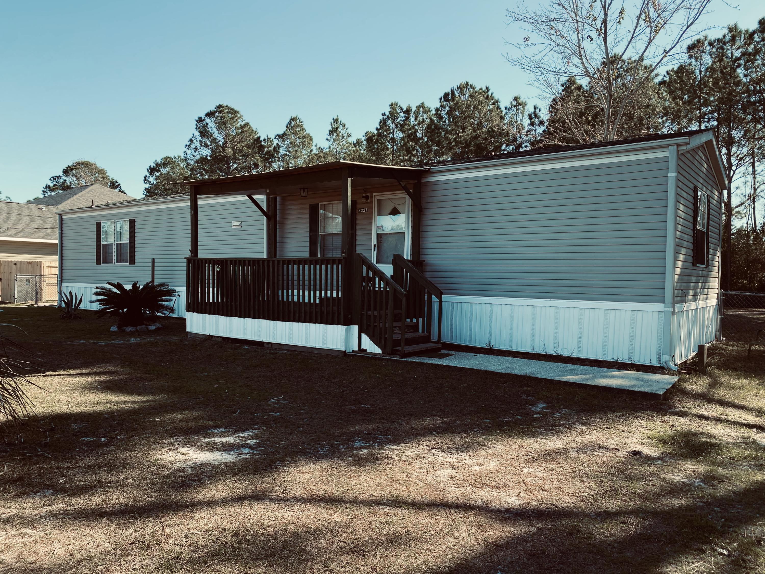 Quaint well maintained mobile home located on .45 of an acre just minutes from the wonderful Navarre Beach. This two-bedroom split floor plan features NEW wood vinyl plank flooring in the living room and master bath. The carport and workshop are easily accessed of the back covered porch. Chain link fence with double gate encompass the back yard. There is an outside sink and shower after a day at the beach. Extra storage (with power) attached to workshop, fire pit and a charming tree house too! Sewer hookup is available. This is would make a great first home or investment home. Schedule your private showing today.