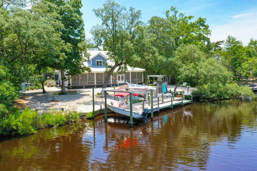 In this charming, private compound on the bayou, you'll find an eclectic collection which includes a fascinating home with spacious screened porch, large workshop building, winsome potting or she shed, dock and boat lift. The property rests on three-quarters of an acre and offers privacy, waterfront and many natural components. Vaulted ceilings are locally-sawn cypress, and the soaring, two-sided stone fireplace features rock from Tennessee. There are marble counters, a cypress kitchen island topped with glass and custom-made glass door knobs. The house is just six years old and features a whole house generator with a 500 gallon buried propane tank and two Rinnai tankless water heaters.