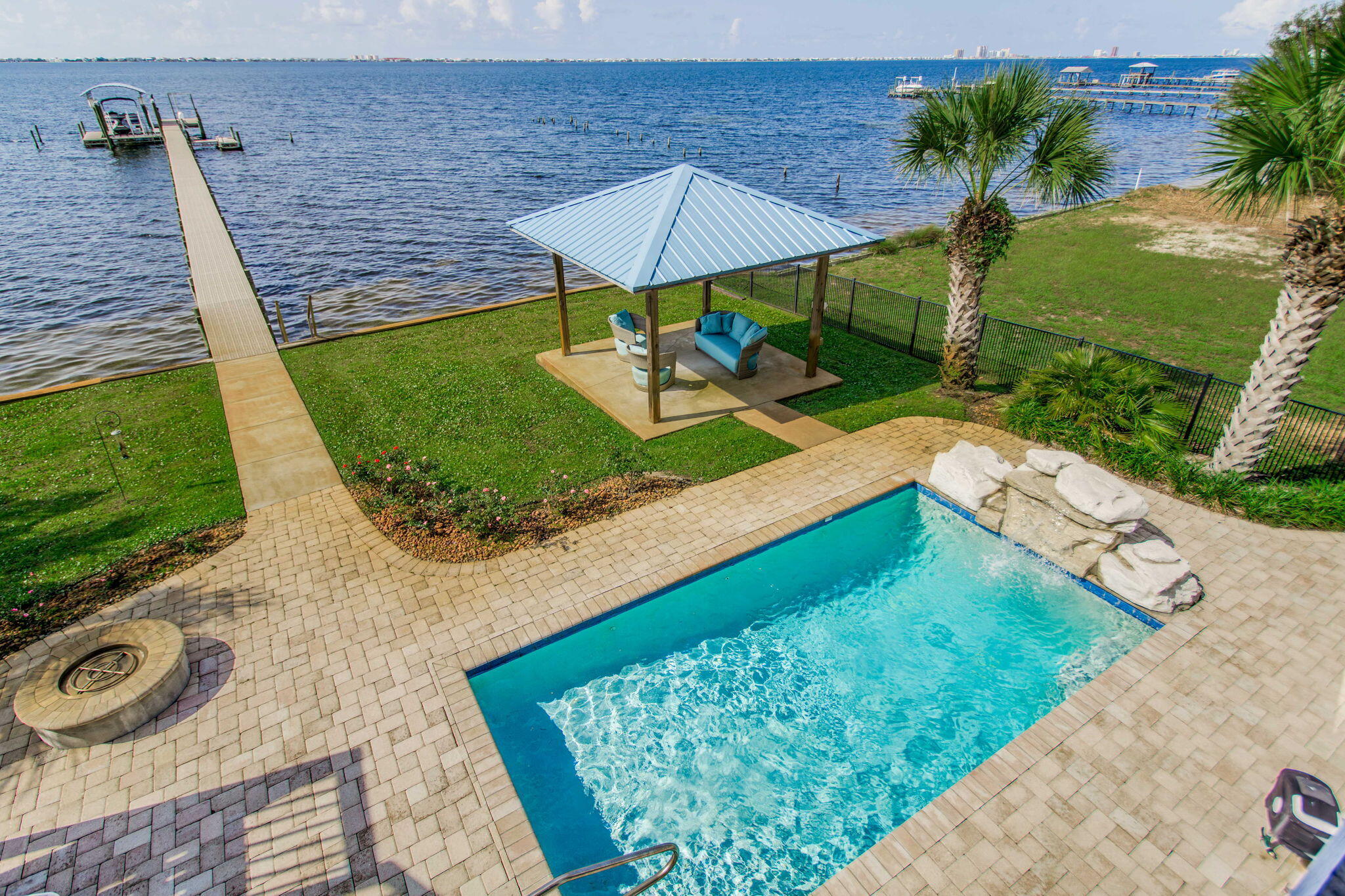 Waterfront luxury in Gulf Breeze - 5-bedroom, 4.5-bath with dock, pool, and elevator: Custom-built waterfront estate offering breathtaking views of the Intracoastal Waterway, featuring a 250-ft pier with boat slip, lift, and two jet ski lifts, vinyl seawall, and new Trex decking. Enjoy resort-style outdoor living with a private pool and rock waterfall, gazebo, and an expansive balcony with built-in outdoor kitchen, gas grill, sink, and custom cabinetry.The main living area boasts a chef's kitchen with maple-glazed cabinetry, blue granite countertops, center island, flat cooktop, and built-in oven. The open floor plan flows into a spacious living room with a gas fireplace, surround sound, and stunning water views. Ten-foot ceilings, crown molding, eight-inch baseboards, Eight-foot solid-core doors, and designer faux finishes throughout add a touch of refined elegance.
The primary suite offers water views, reclaimed wide-plank pine floors, trey ceiling, and a spa-inspired bath with walk-in travertine shower, whirlpool tub, Kohler fixtures, and his-and-hers walk-in closets. You will also find an additional 2 bedrooms, full bathroom with dual vanities plus a half bath for visitors.
The lower level functions as a complete guest or in-law suite with two bedrooms, two bathrooms, office, kitchenette, living area, and custom built-ins. Access both levels via a custom iron staircase or a cherry wood-paneled elevator.
Additional features include:
* Wet bar and entertainment center downstairs
* Jack-and-Jill bath for guest bedrooms
* Cypress ceilings and IPE decking on the porch
* Surround sound inside and on decks
* Hurricane shutters for all windows and doors
* Mahogany front door
* Ample storage throughout
Located just two blocks from a boat launch and minutes from top-rated schools, shopping, and Pensacola Beach. Enjoy southern exposure, cooling Gulf breezes, and unforgettable sunrises and sunsets from your own backyard. This is coastal living at its finest!