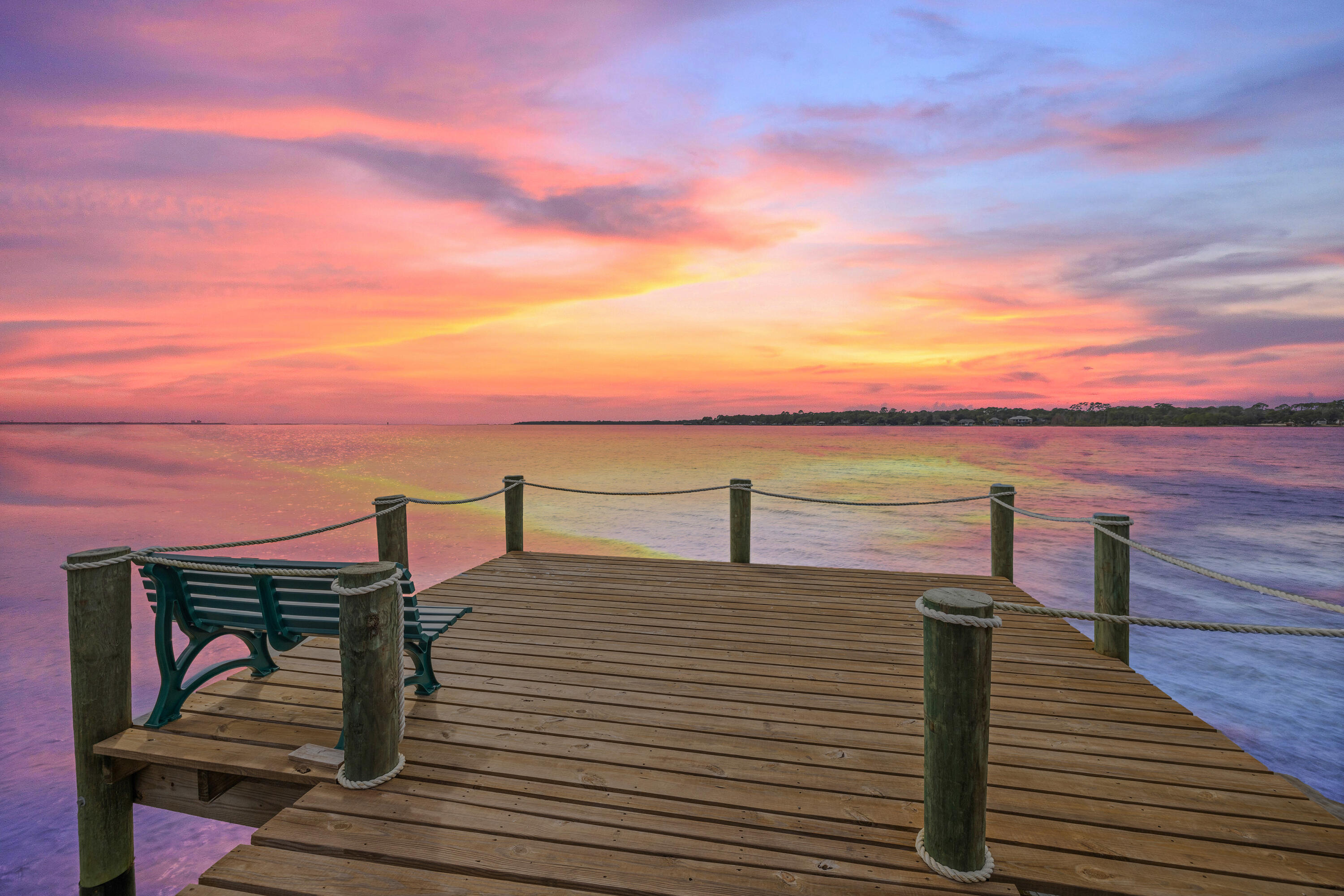 Whether you are searching for the busy life of live entertainment, optional amenities, and water access or you want to sit back and watch a sunset, this 2 bedroom fully furnished property may be the perfect fit! Thriving as an active Air BNB, the complex allows for short or long-term rentals and is in close proximity to Eglin Airforce Base and Destin, plus numerous shops, restaurants and the local marina! The neighborhood of Bluewater Bay also offers attractions for members (see home owners association for details on how to become a member) such as golf, tennis, pickle ball, and swim and is golf cart friendly. The heart of the unit is found between the kitchen to spacious main living area and is perfect for large gatherings or entertaining. Both the main living area and primary bedroom maintain a water view and patio access through sliding glass doors making for an easy indoor to outdoor flow! The kitchen features granite countertops and stainless steel appliances with a charming serving window and there is vinyl flooring throughout. The primary bedroom has a King bed set with an accent shiplap wall. The primary en-suite showcases double sinks, granite countertops, whit shaker cabinets and a large tiled shower. With a split floorplan, the secondary bedroom also has a King bed set and maintains a half bathroom.
Relax on your back porch area that is open to the common grounds and dock for bay access. The complex faces West, making for incredible sunsets year around!